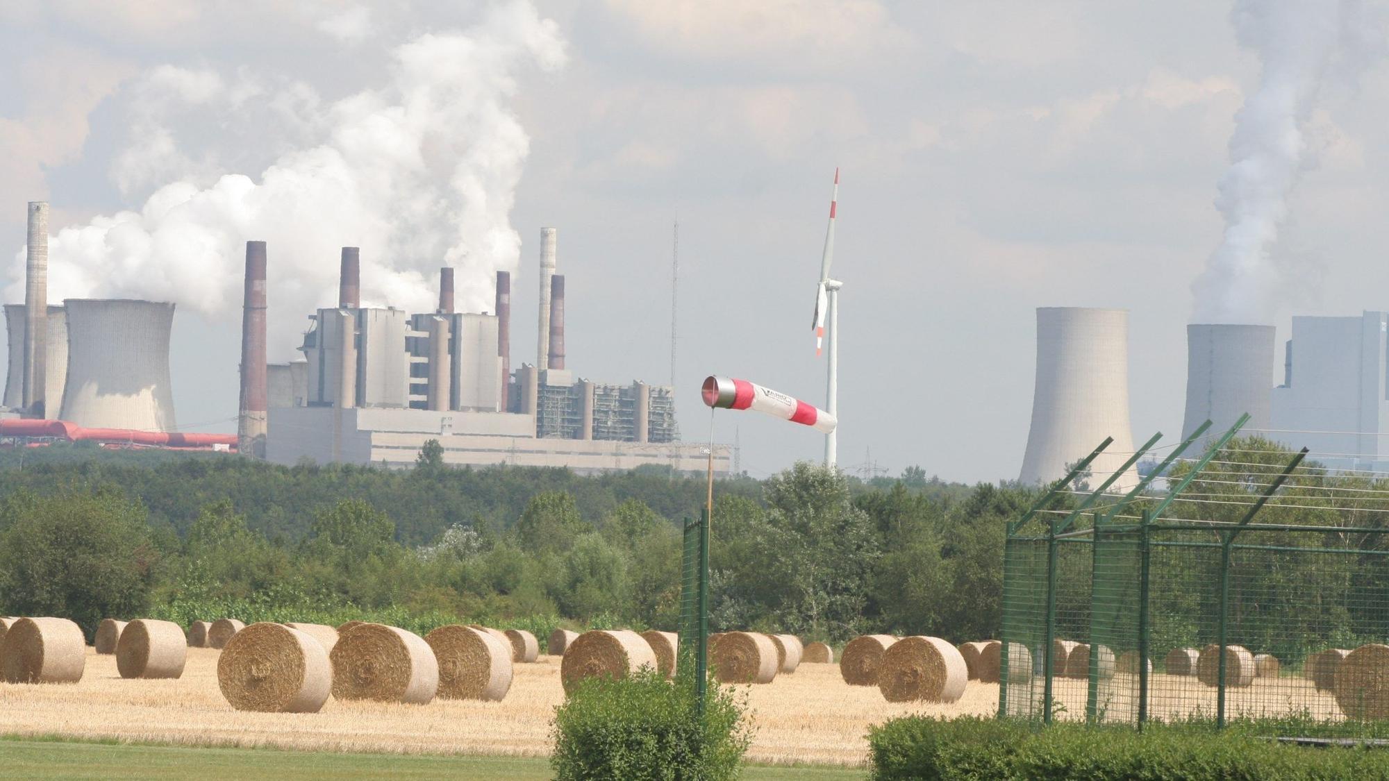 Das Bild zeigt ein Feld mit Strohballen vor der Kraftwerkskulisse.
