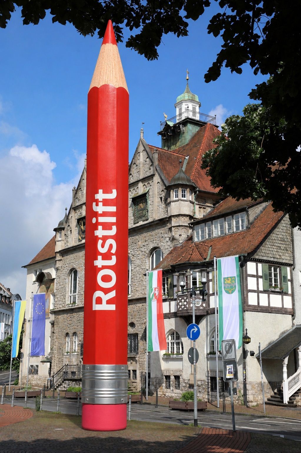 Die Fotomatage zeigt einen roten Stift vor dem Rathaus.