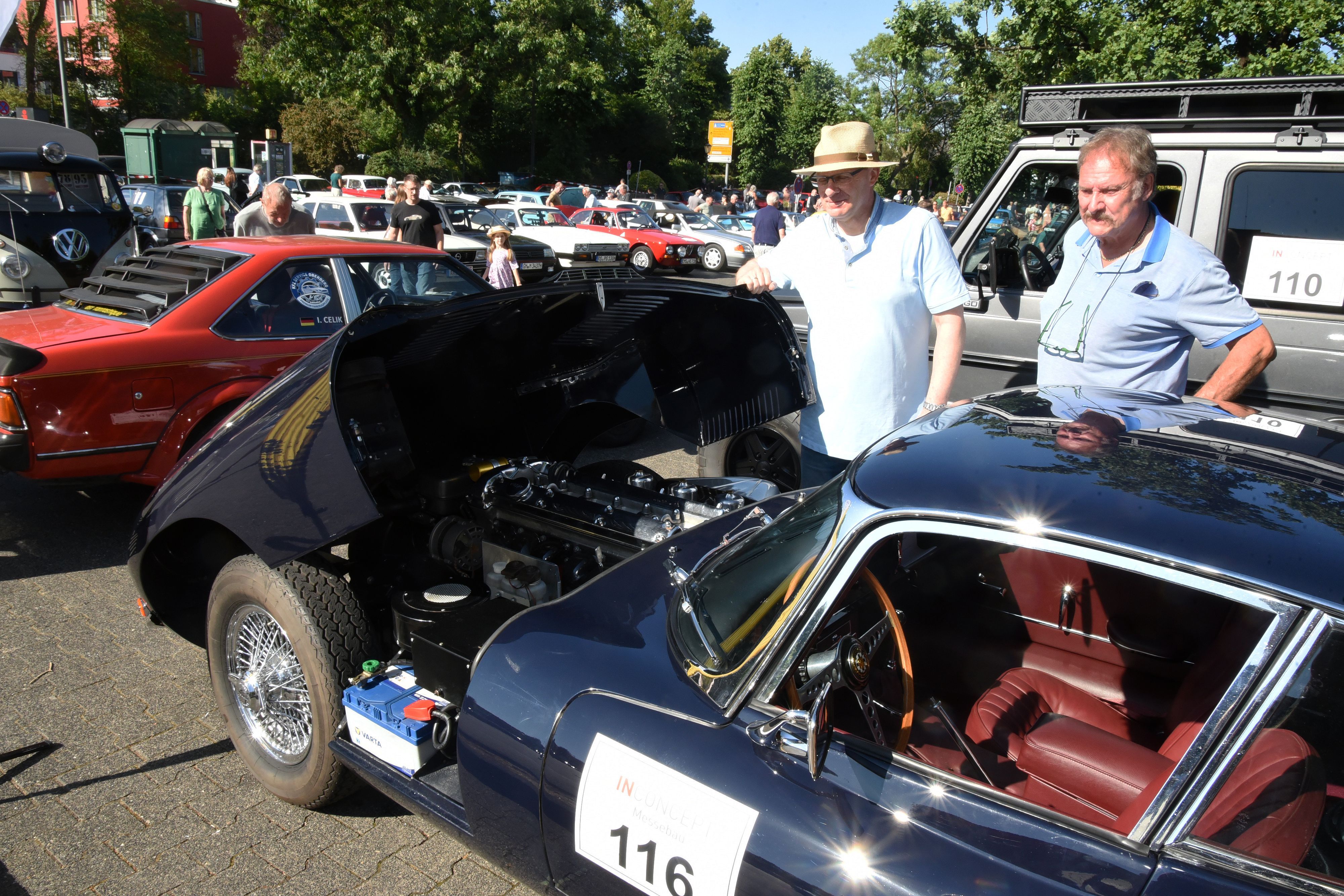 Zahlreiche Oldtimer-Autos stehen auf einem Platz, ein Jaguar hat die Motorhaube geöffnet.