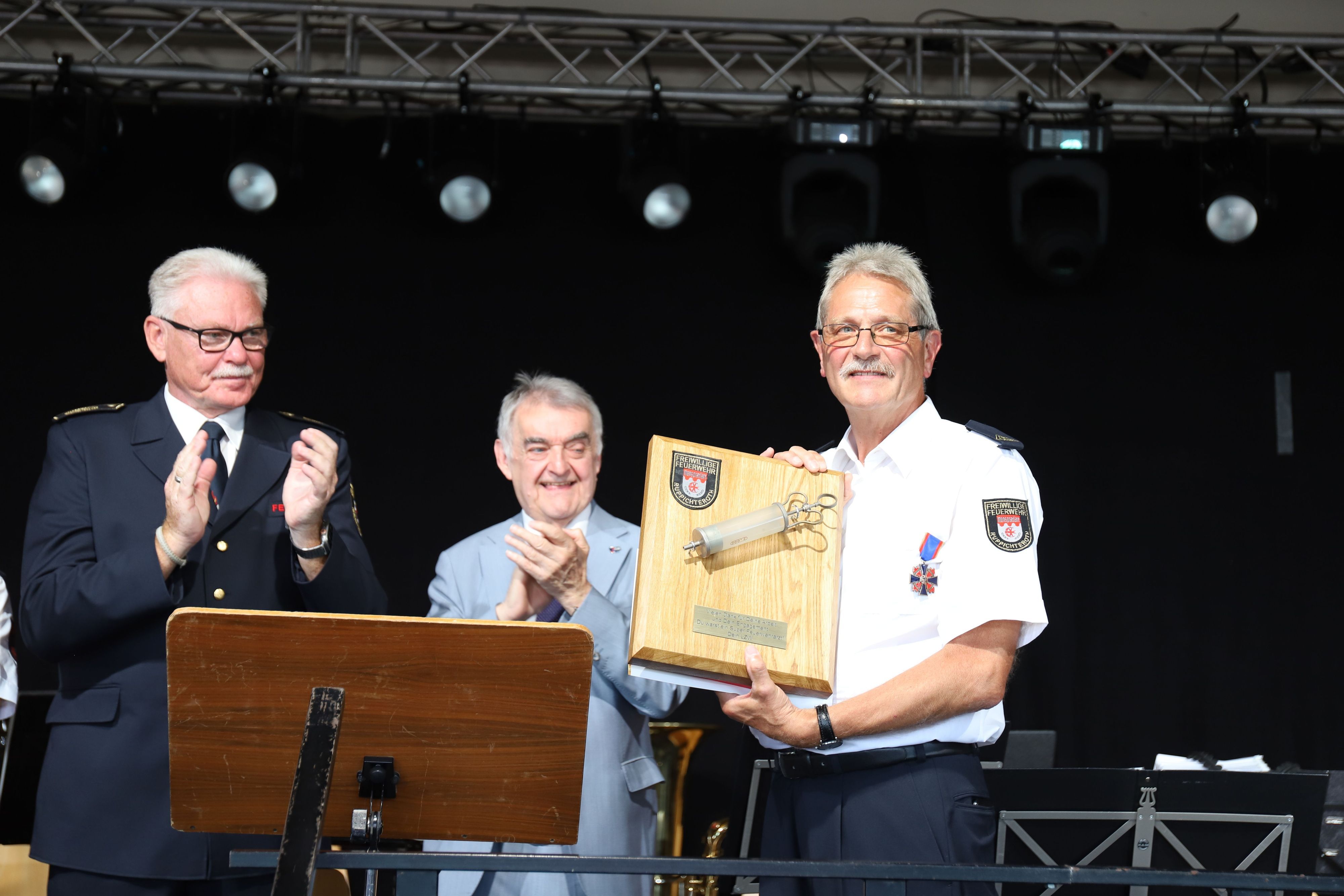 Feuerwehrarzt Dr. Herbert Broich (r.) erhielt vom Löschzug Winterscheid zum Abschied eine alte, große Spritze. Kreisbrandmeister Stefan Gandelau (l.) und Innenminister Herbert Reul (M.) applaudieren.