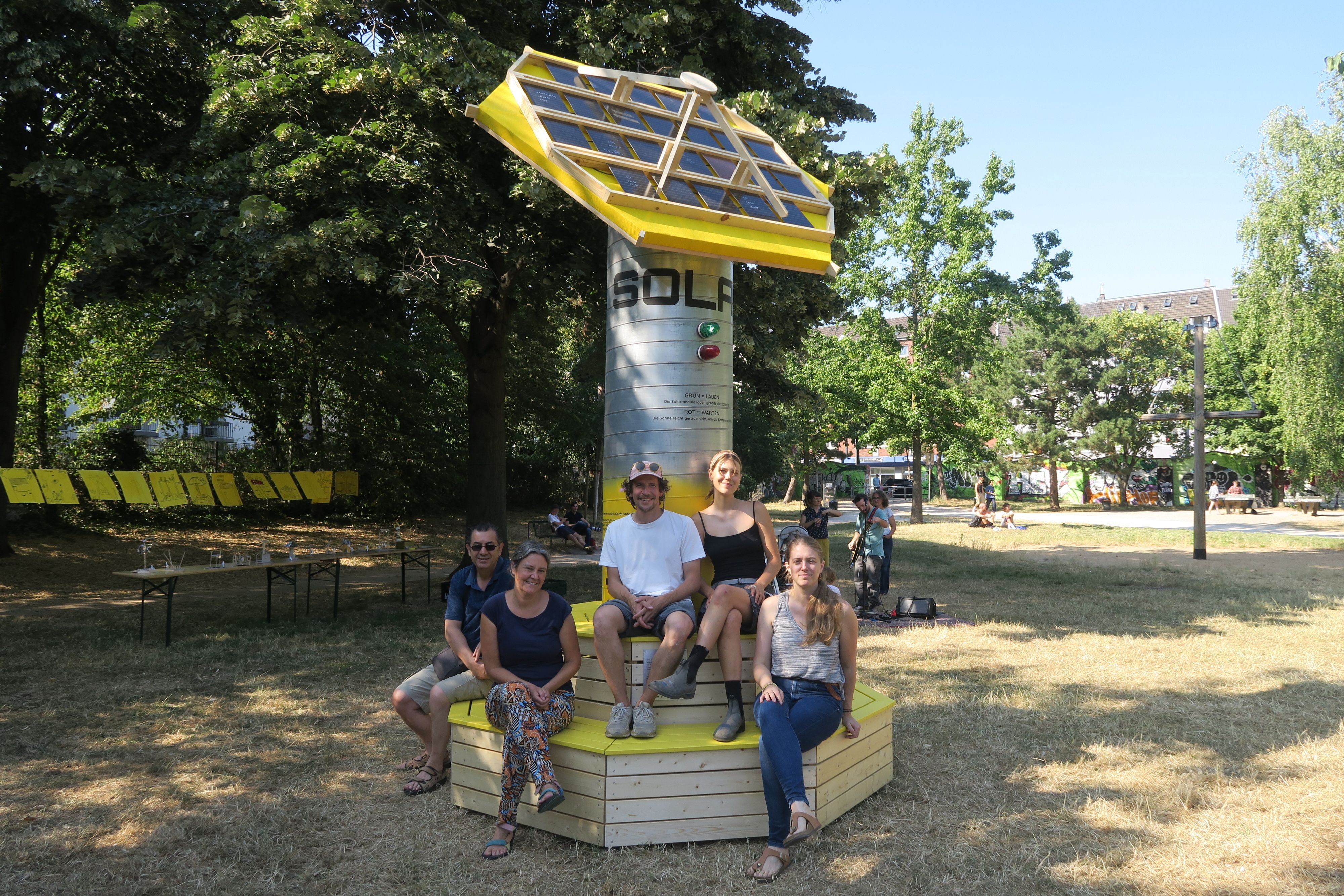 Fünf Menschen sitzen auf Sitzbänken, die eine Solarskulptur umgeben.