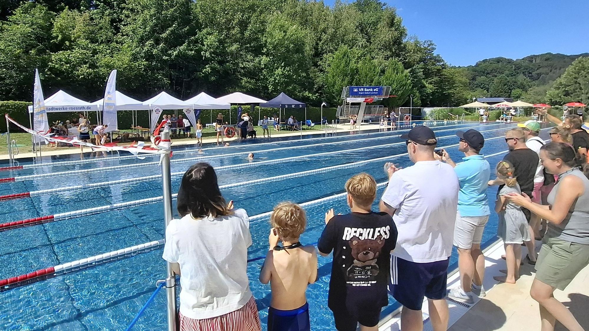 Menschen stehen am Rand des Schwimmbeckens im Freibad und feuern die Schwimmer an.