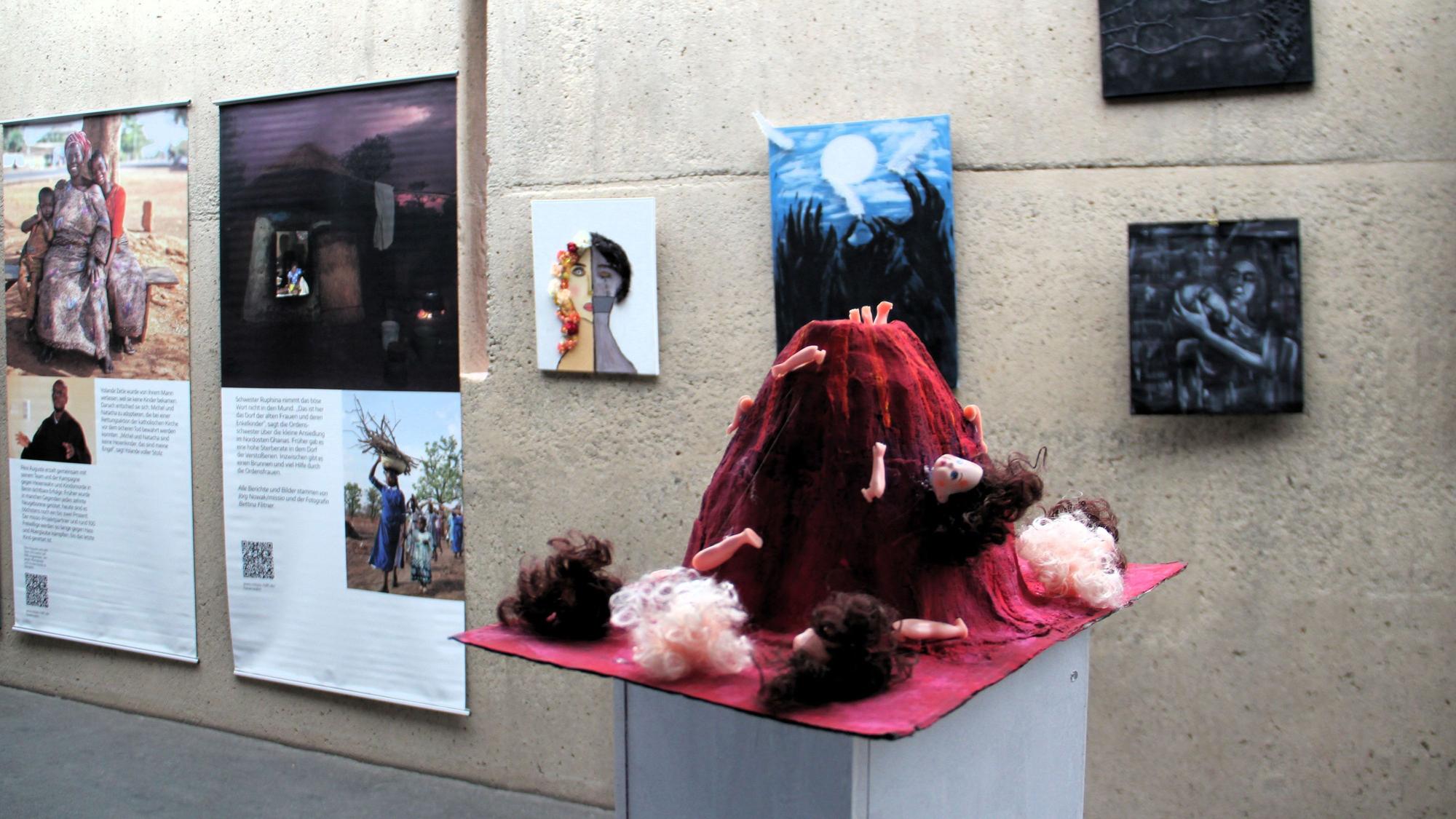An einer Wand hängen Bilder und erklärende Texte, auf einem Podest ist eine Installation aus Puppen zu sehen.