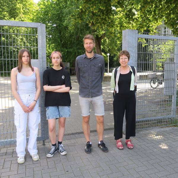 Zwei Schülerinnen, ein Lehrer und eine Lehrerin stehen vor dem offenen Schultor der Gesamtschule in Bocklemünd.