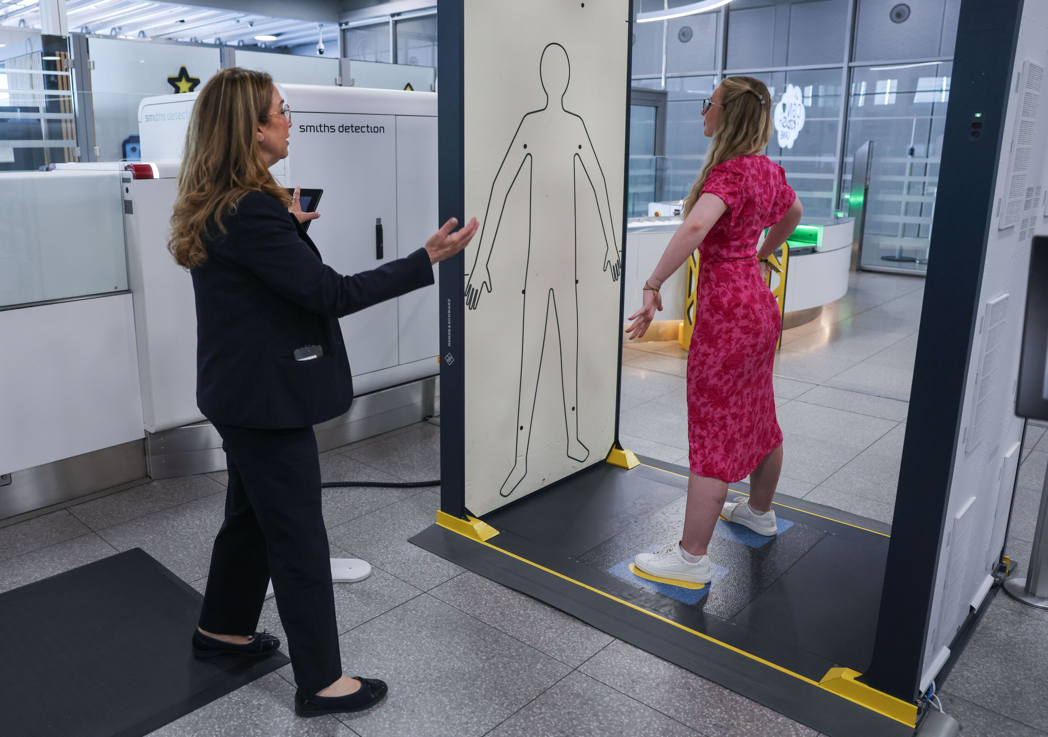 Die Mitarbeiterin einer Sicherheitsfirma leitet im Sicherheitsbereich am Flughafen Köln/Bonn eine Reisende in einen Körperscanner.