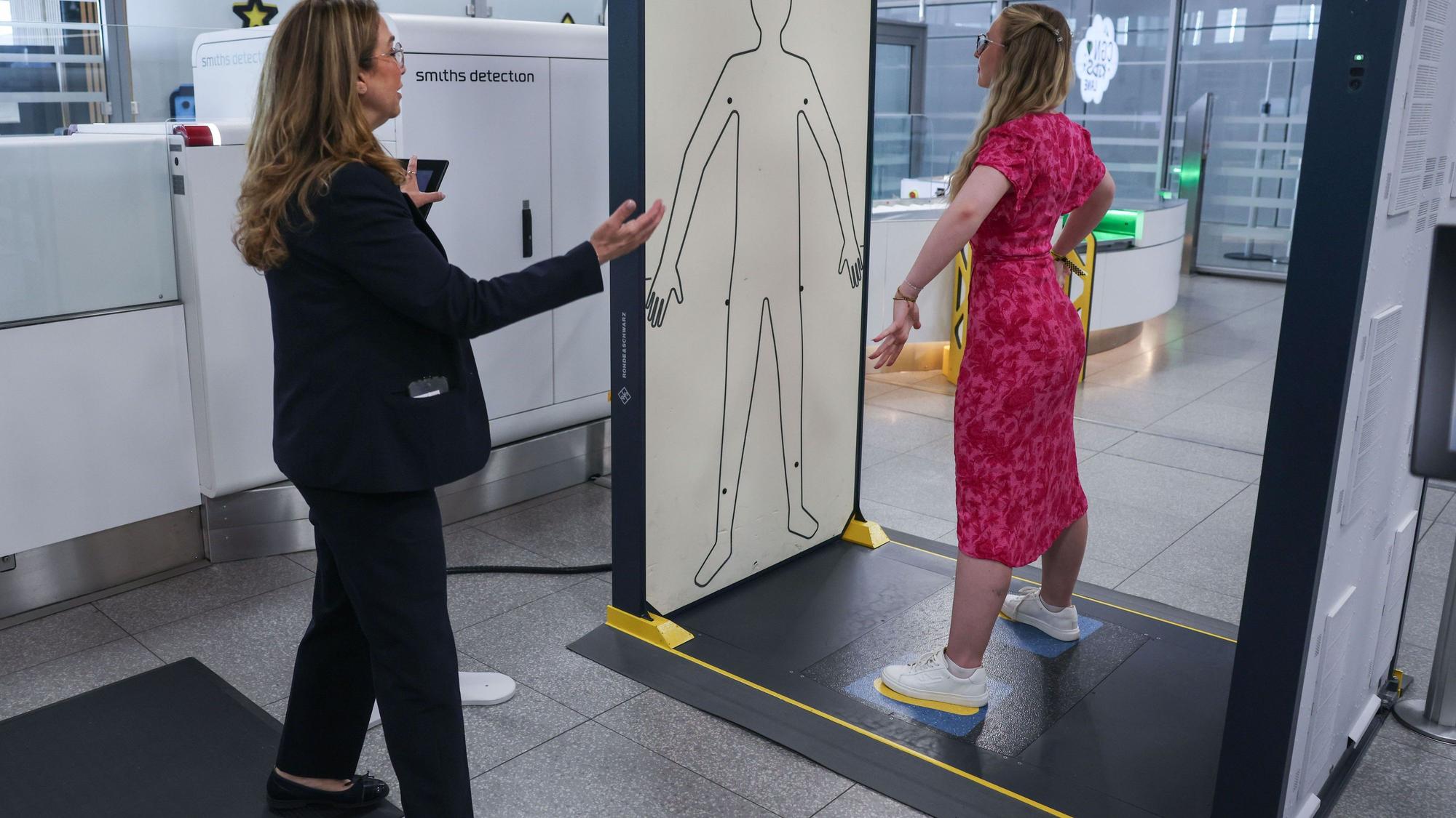 Die Mitarbeiterin einer Sicherheitsfirma leitet im Sicherheitsbereich am Flughafen Köln/Bonn eine Reisende in einen Körperscanner.
