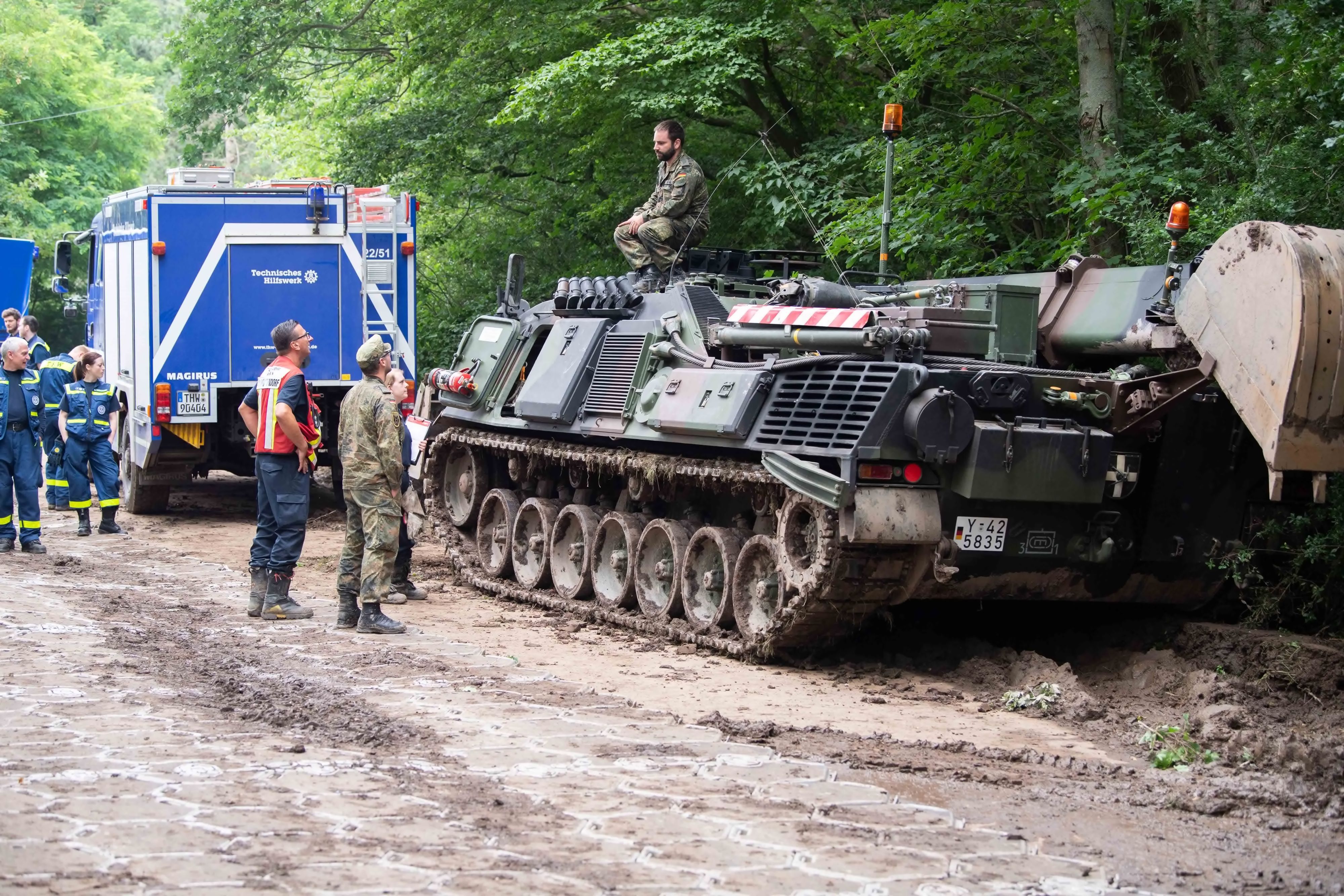 Das Bild zeigt Soldaten im Gespräch mit Mitarbeitenden des THW. Der Soldat sitzt an der Steinbachtalsperre auf einem Panzer.