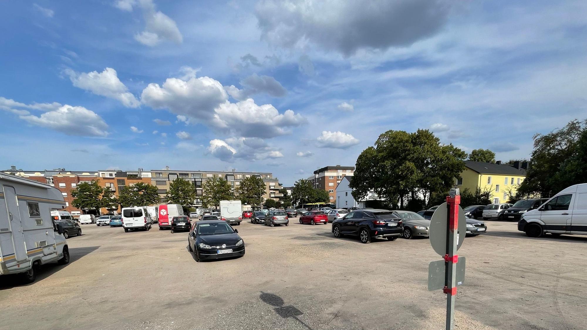 Auf dem Platz stehen Autos, Wohnmobile und Transporter. Am Rand sind Bäume platziert.