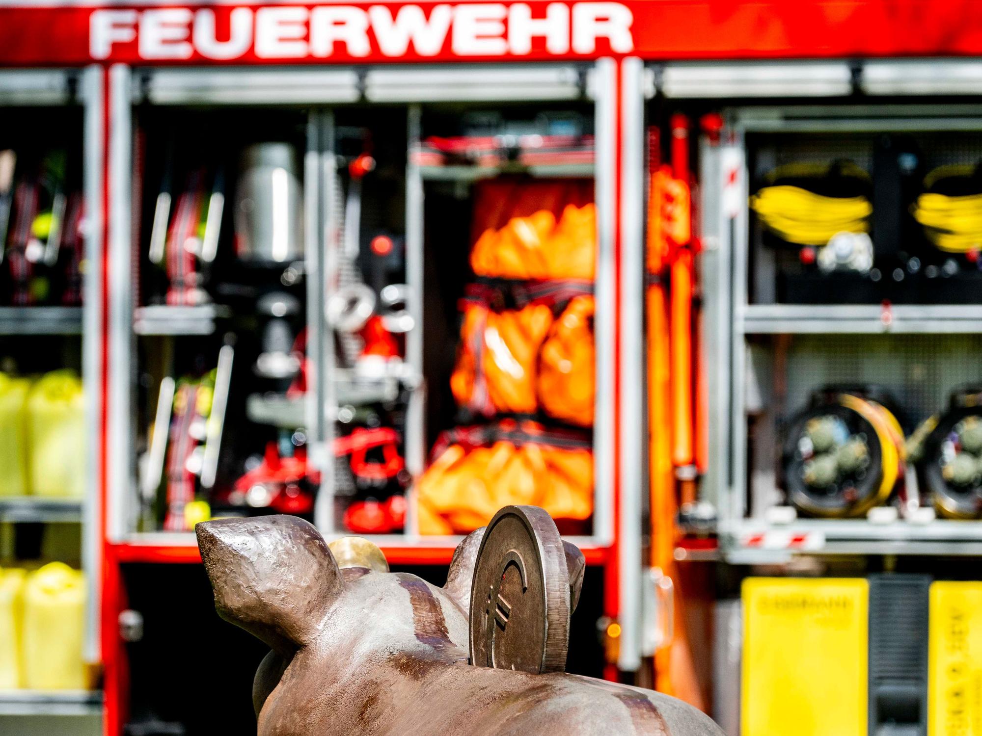 Das Bild zeigt ein Sparschwein vor einem Feuerwehrfahrzeug.
