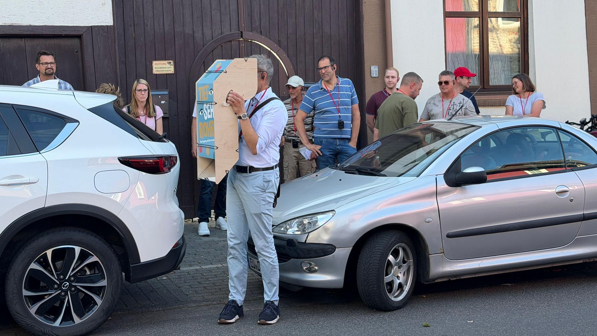 Ein Teilnehmer, der zwischen zwei geparkten Autos steht, hält sich den Apparat vor die Augen.