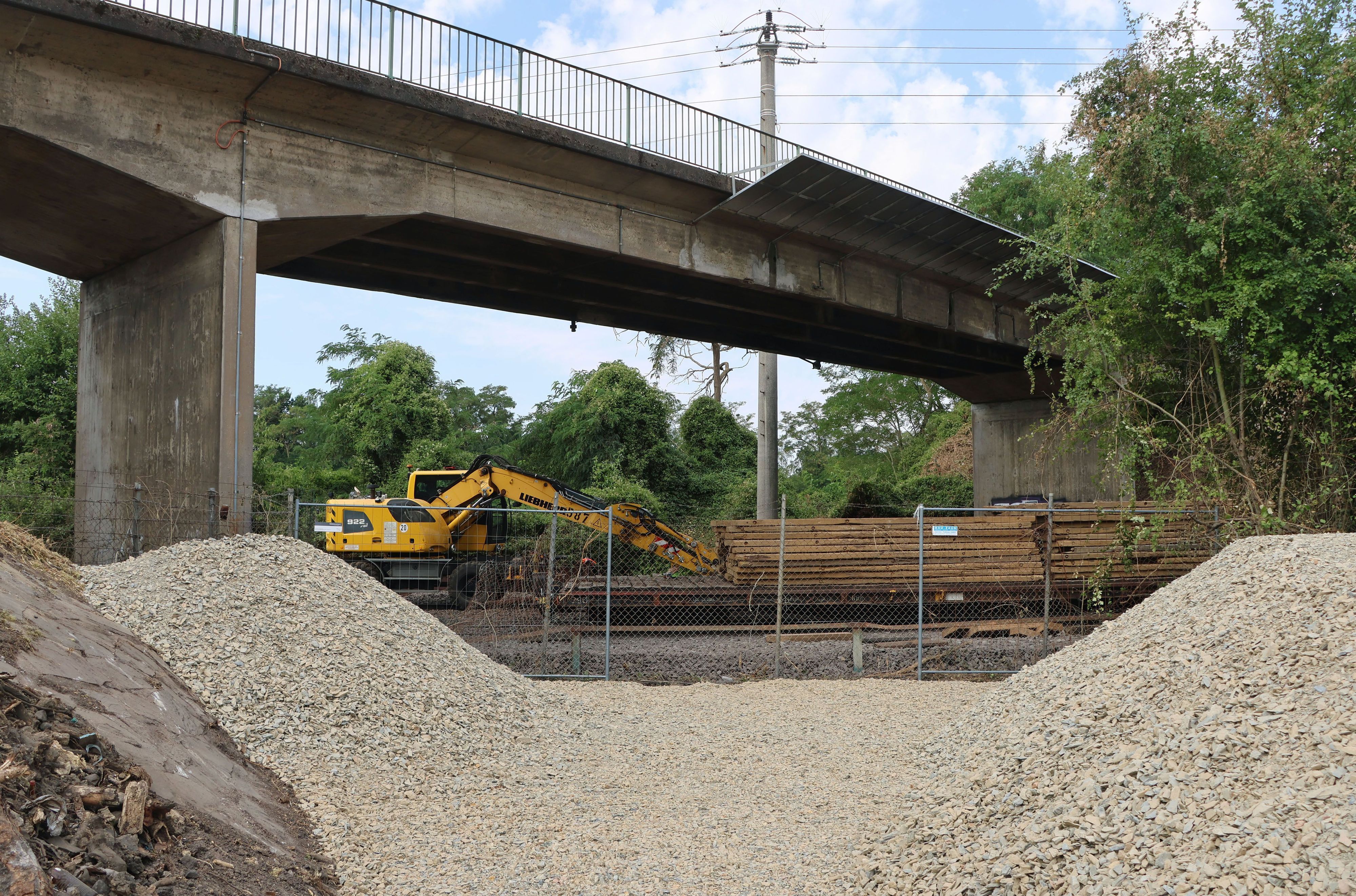 Auf dem Foto sind eine Brücke, ein Bagger, Bauzäune und Schotterhaufen zu sehen.
