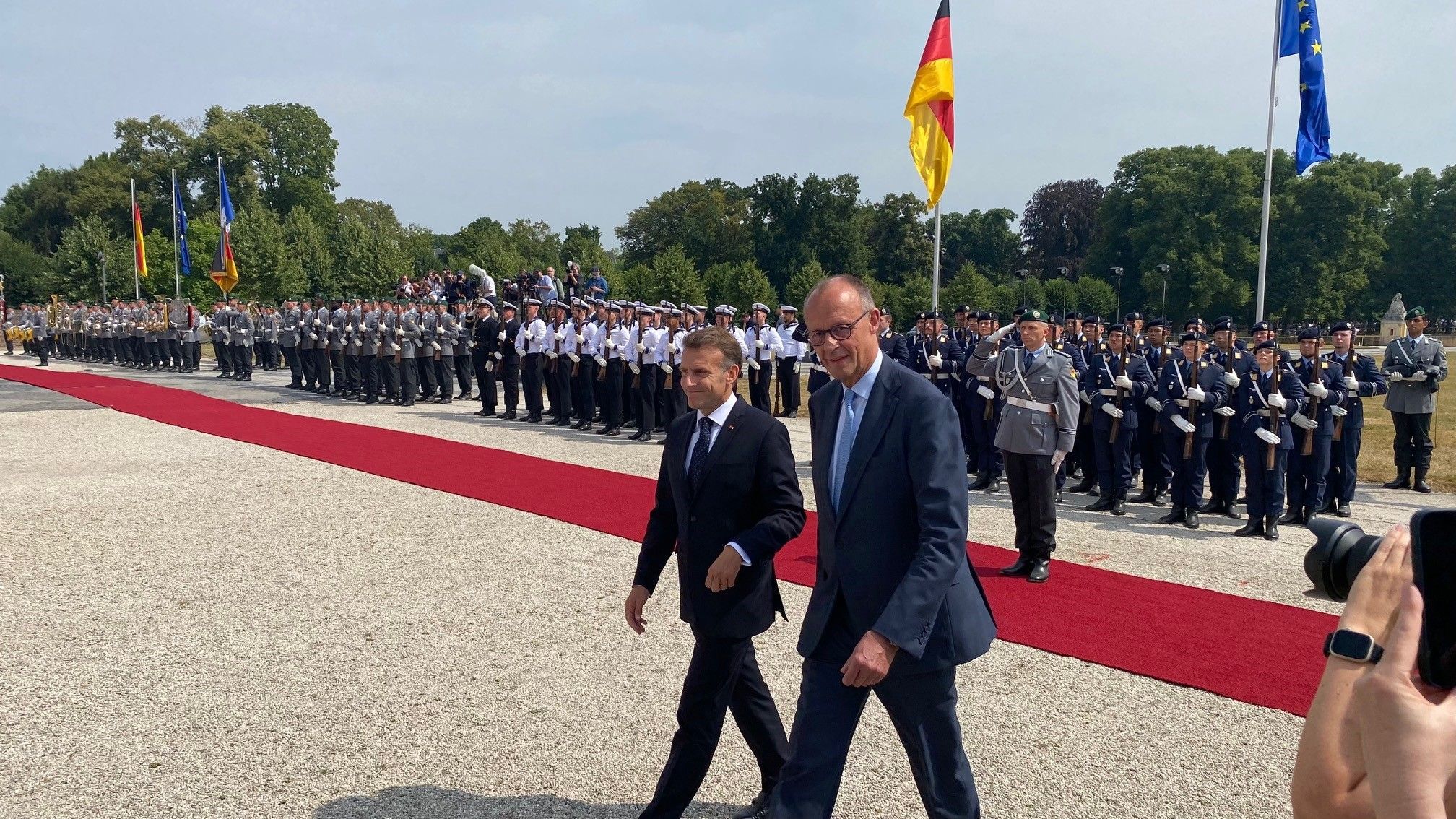 Zu sehen sind Bundeskanzler Friedrich Merz und der französische Präsident Emmanuel Macron sowie im Hintergrund Soldaten.