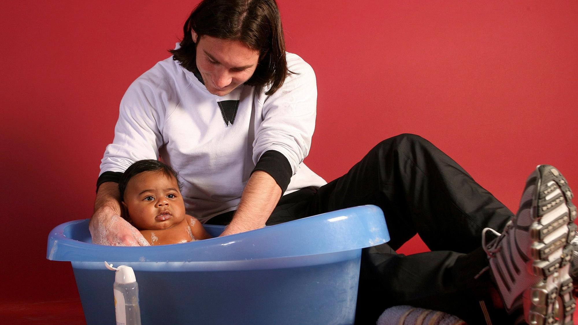 Lionel Messi badet ein Baby in einer Plastikwanne.
