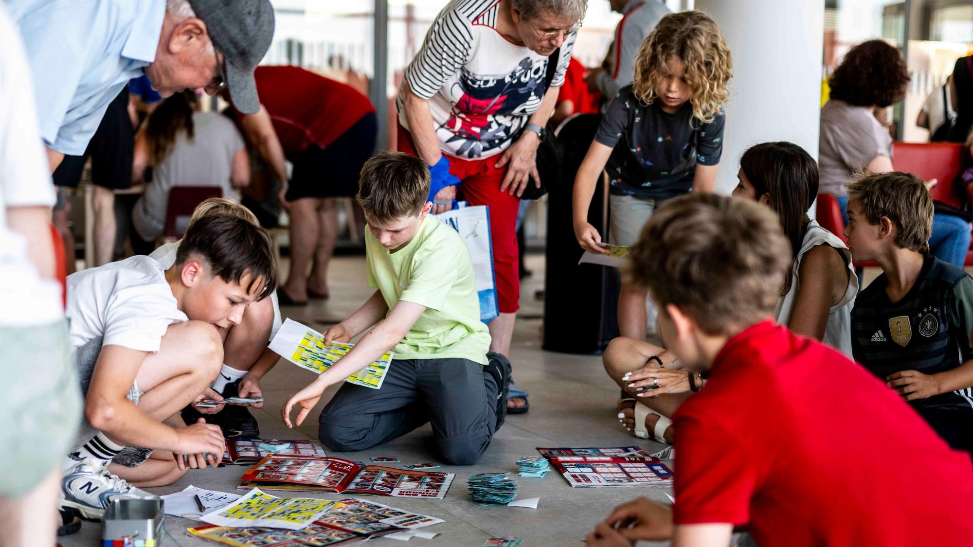 Kinder kauern auf dem Boden, wo sie ihre Sammelbilder ausgebreitet haben.