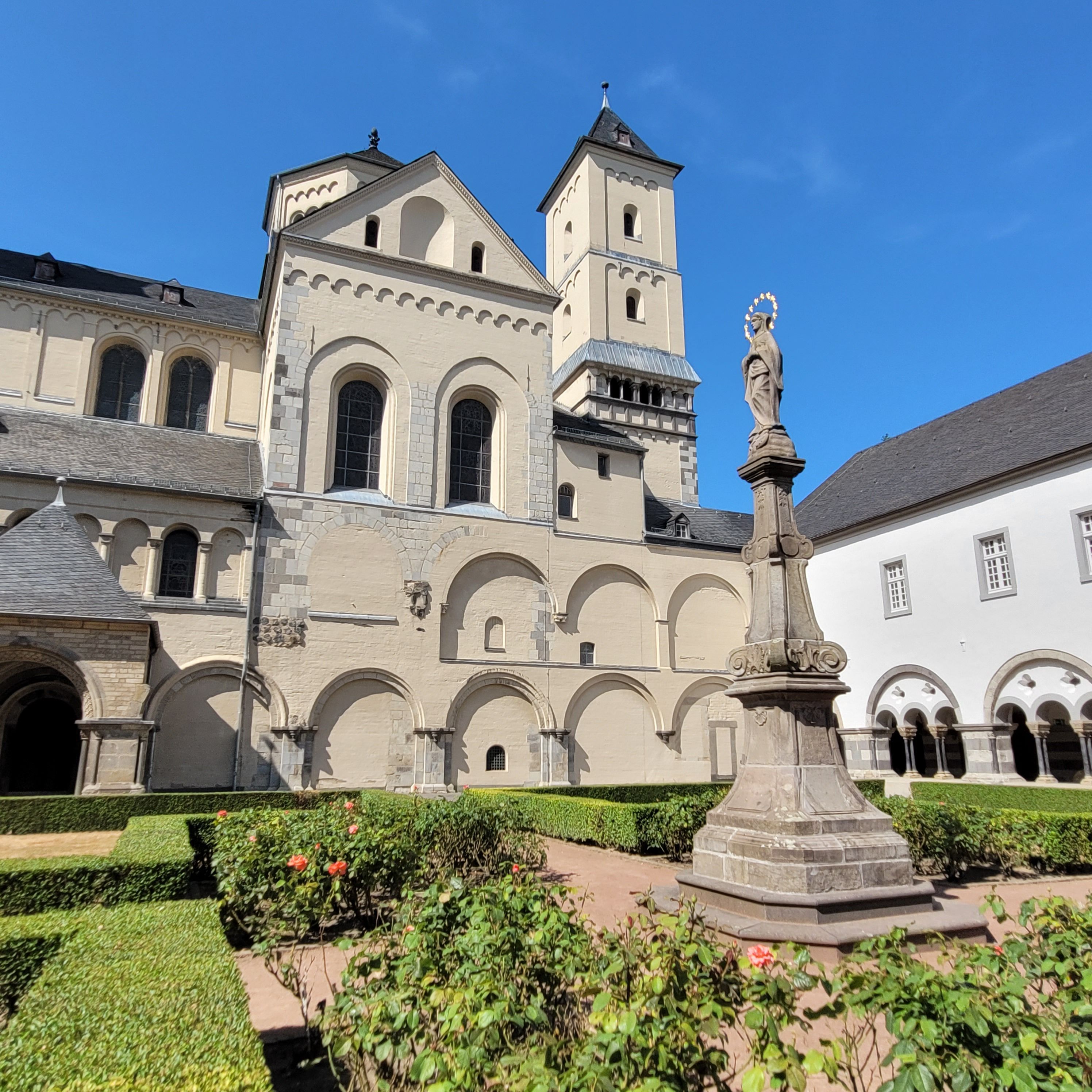 Im Vordergrund eine Marienstatue auf einer Säule, im Hintergrund eine Kirche.