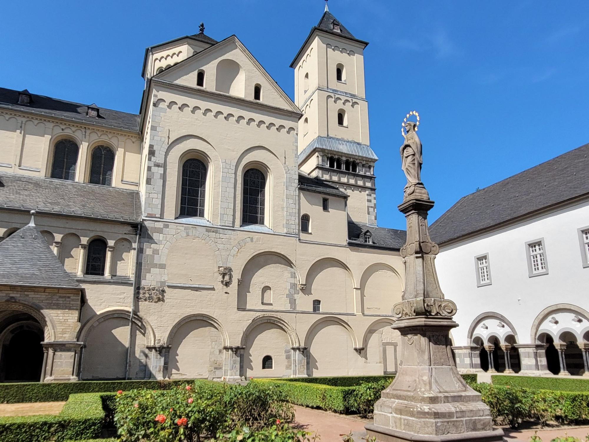 Im Vordergrund eine Marienstatue auf einer Säule, im Hintergrund eine Kirche.