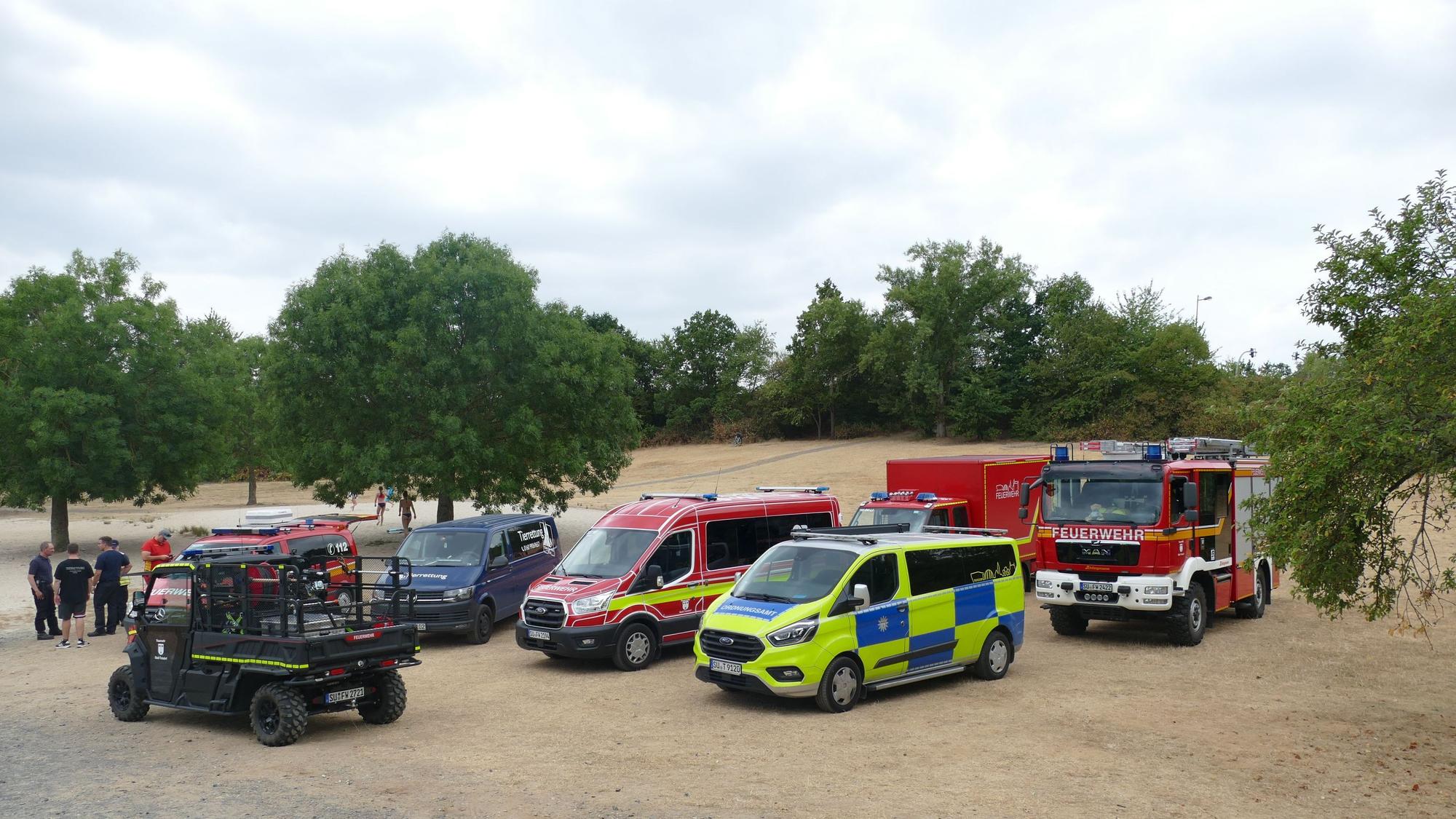 Fahrzeuge von Feuerwehr, Ordnungsamt und DLRG am Ufer eines Baggersees.