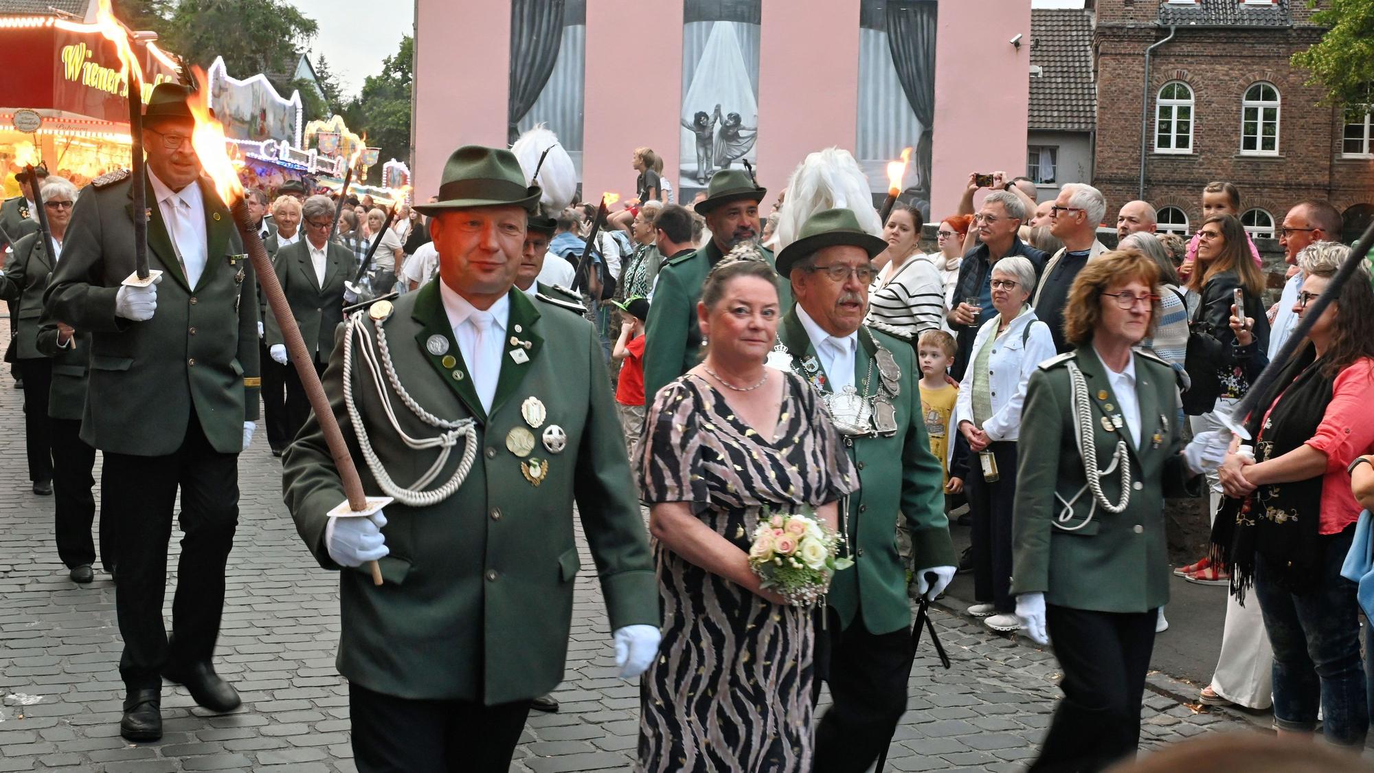 Schützen in Uniform und mit Fackeln marschieren durch die Stadt.