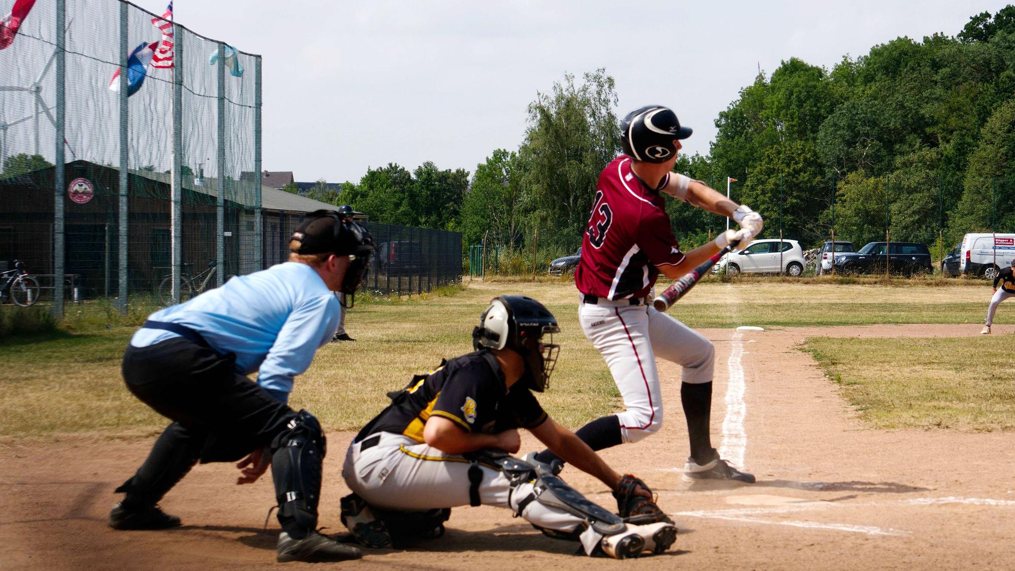 Ein Baseballspieler schlägt am Ball vorbei, der vom Catcher gefangen wird. Dahinter steht der Umpire.