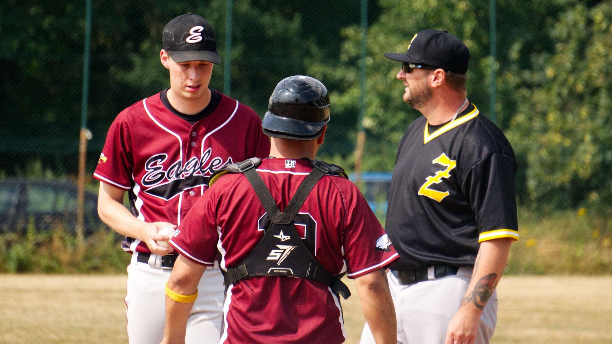 Der Trainer unterhält sich mit seinem Pitcher, der Catcher hört zu.