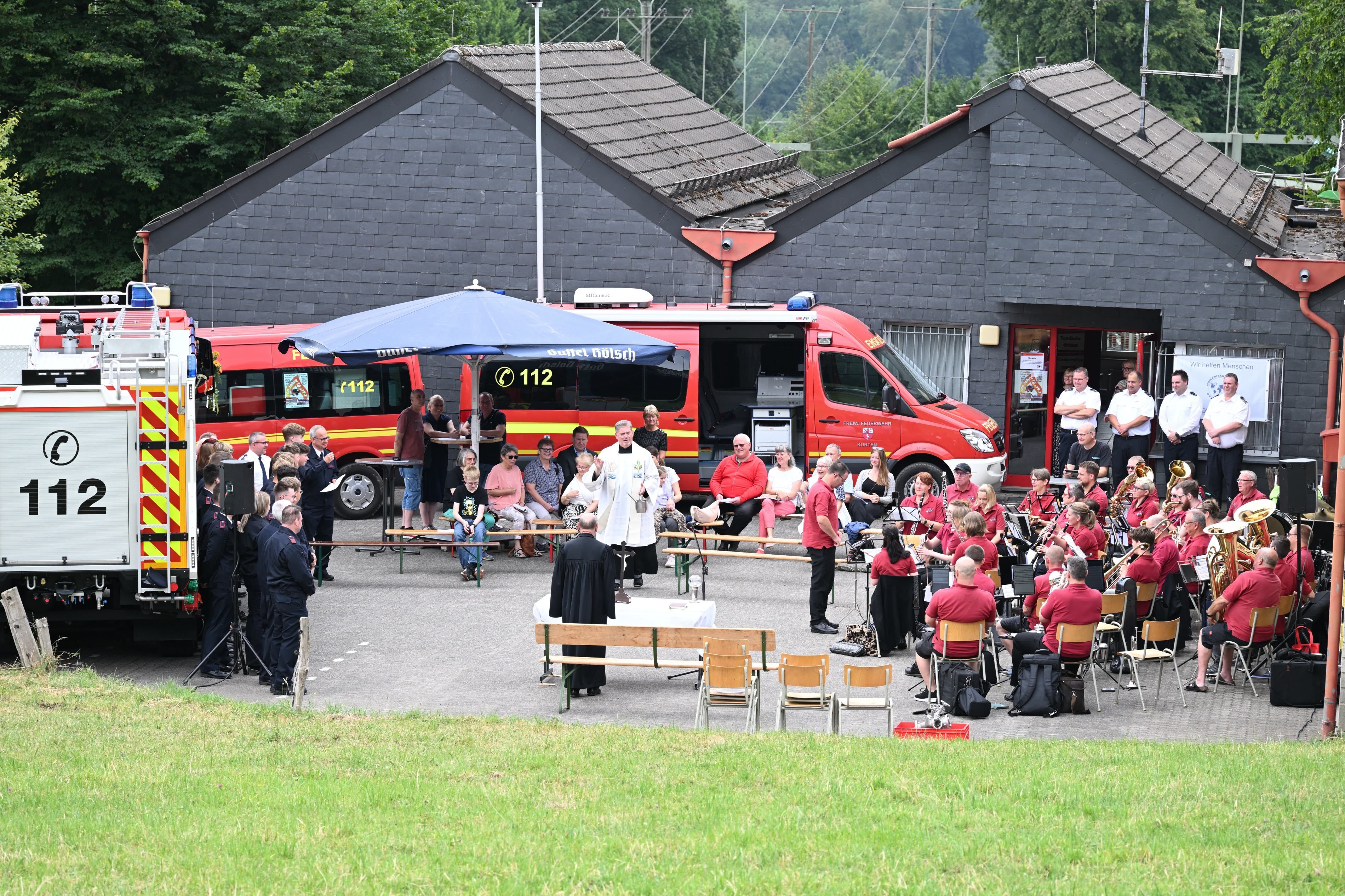 Zu sehen ist das Fest einer Feuerwehreinheit mit einem Pfarrer, der gerade spricht.