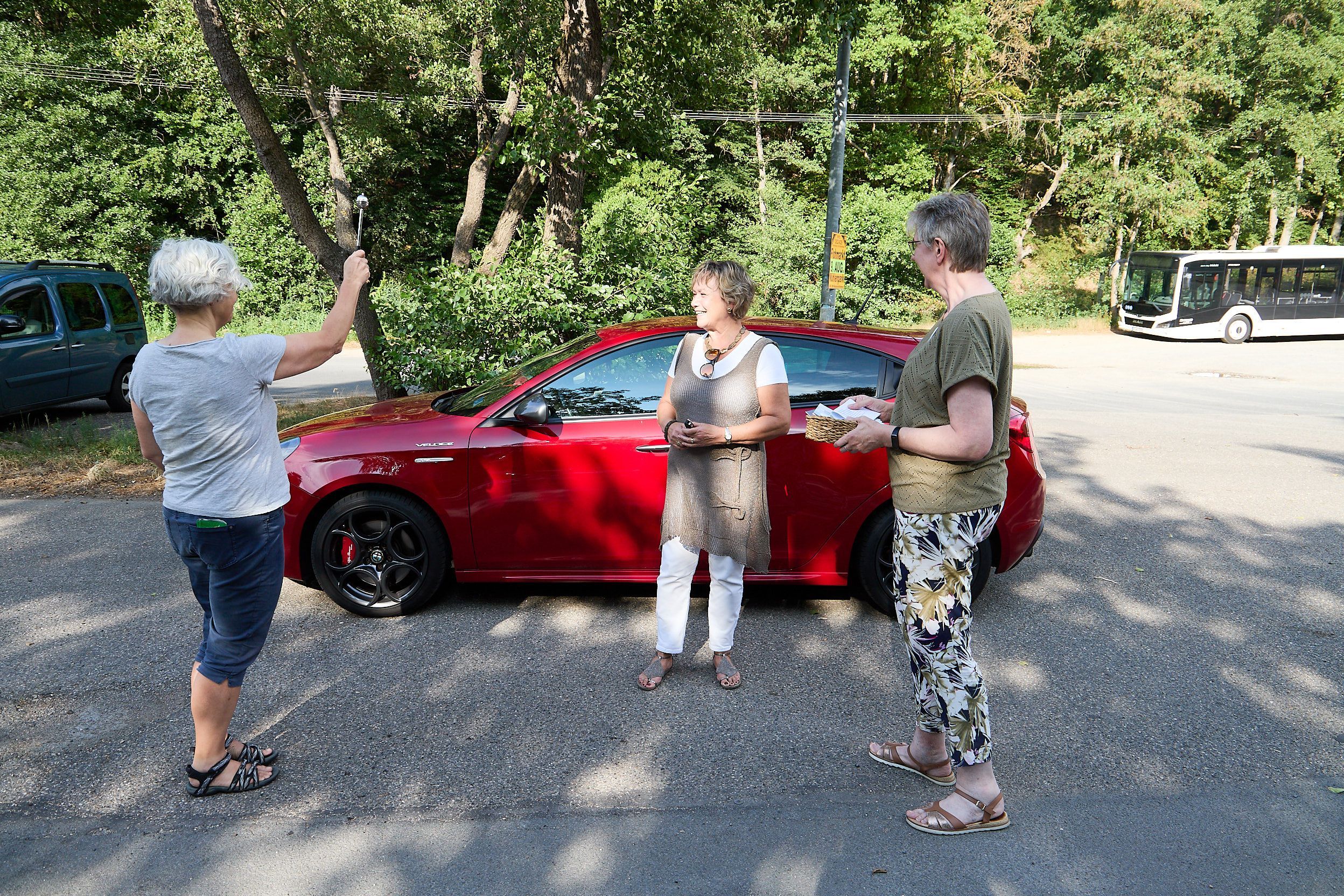 Pfarrerin Susanne Salentin spendet den Segen für zwei Frauen, im Hintergrund steht ein rotes Auto.