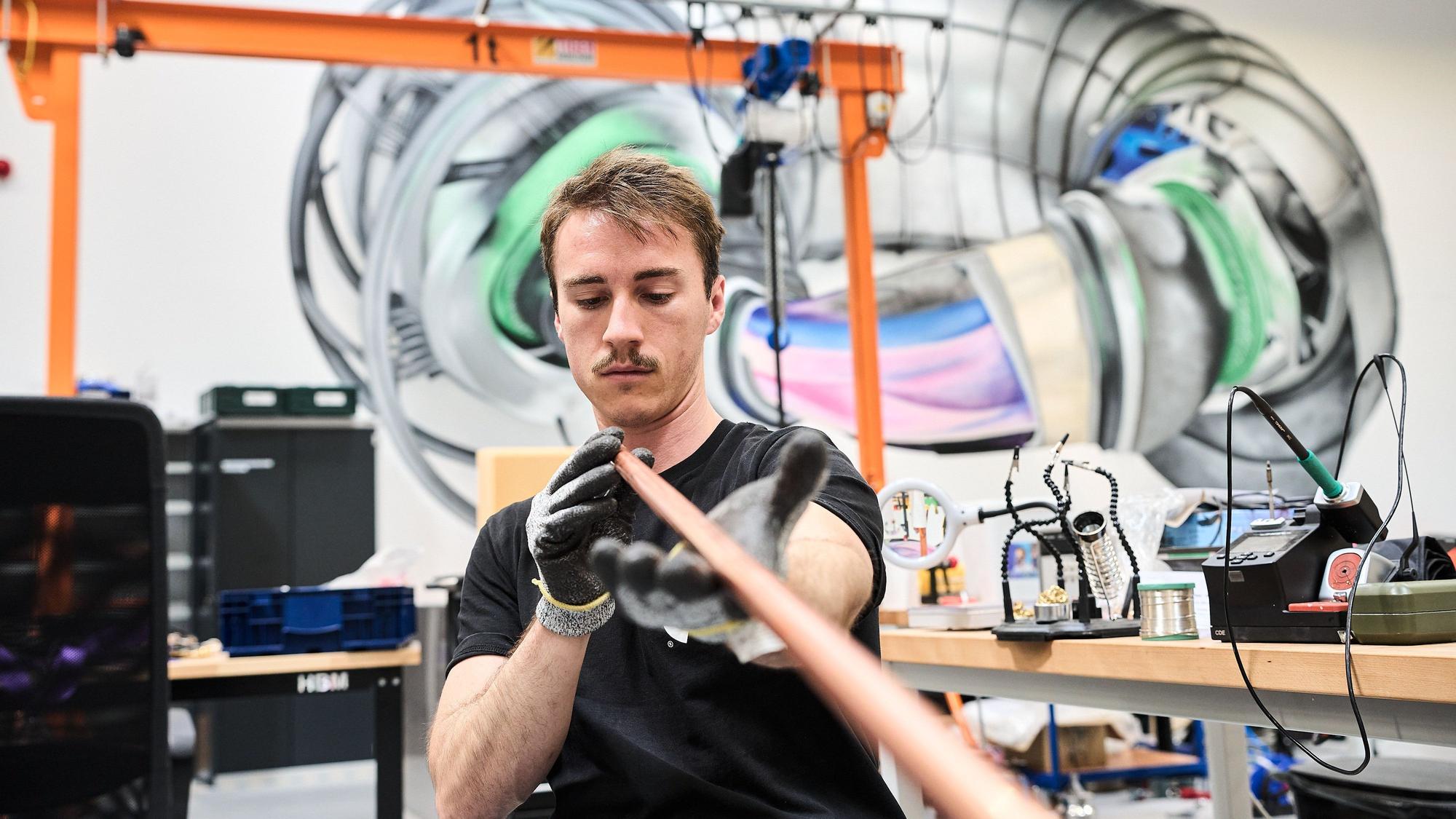 Ein Mitarbeiter von Proxima Fusion in einer Werkstatt des Start-ups. Im Hintergrund ein Modell eines Einschlussmagneten.