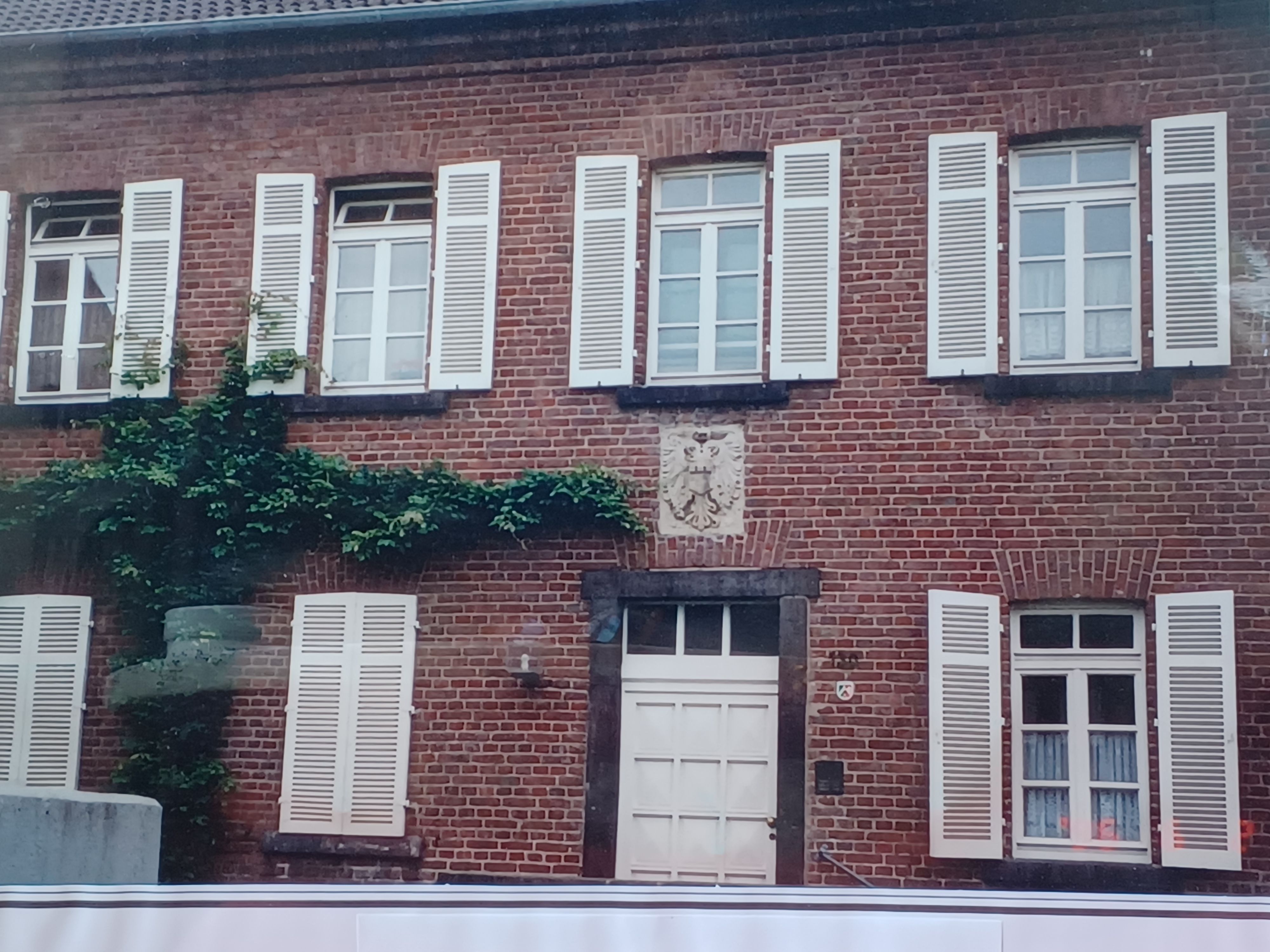 Die Fenster eines zweigeschossigen Backsteingebäudes haben weiße Fensterläden.