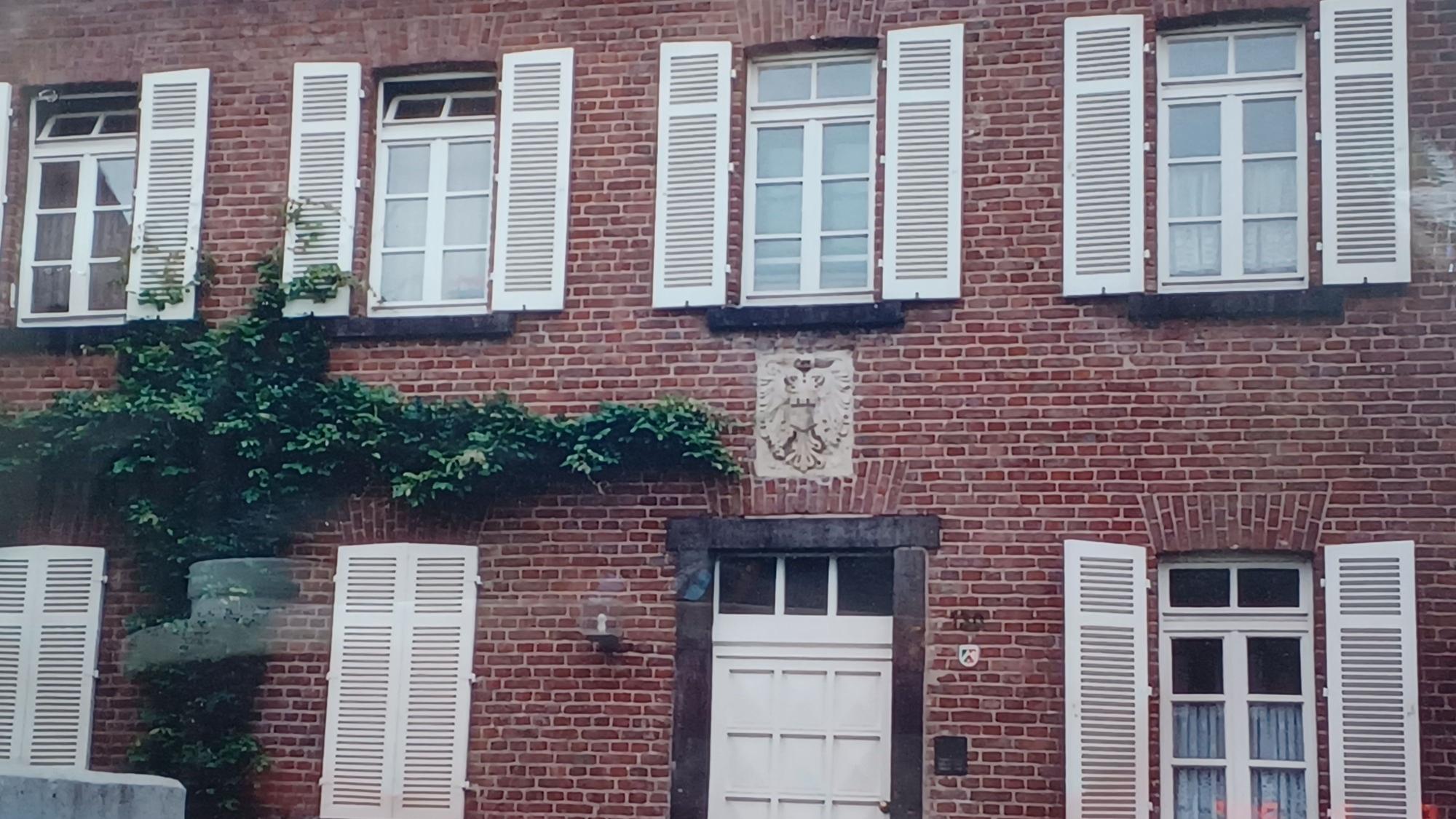 Die Fenster eines zweigeschossigen Backsteingebäudes haben weiße Fensterläden.