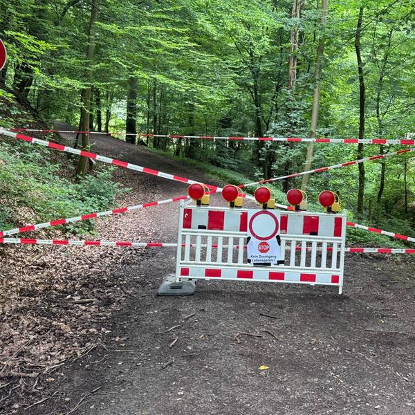Eine weiß-rote Absperrbake vor einem Wanderweg. Darauf ein Schild mit der Warnung: "Kein Durchgang. Lebensgefahr!"