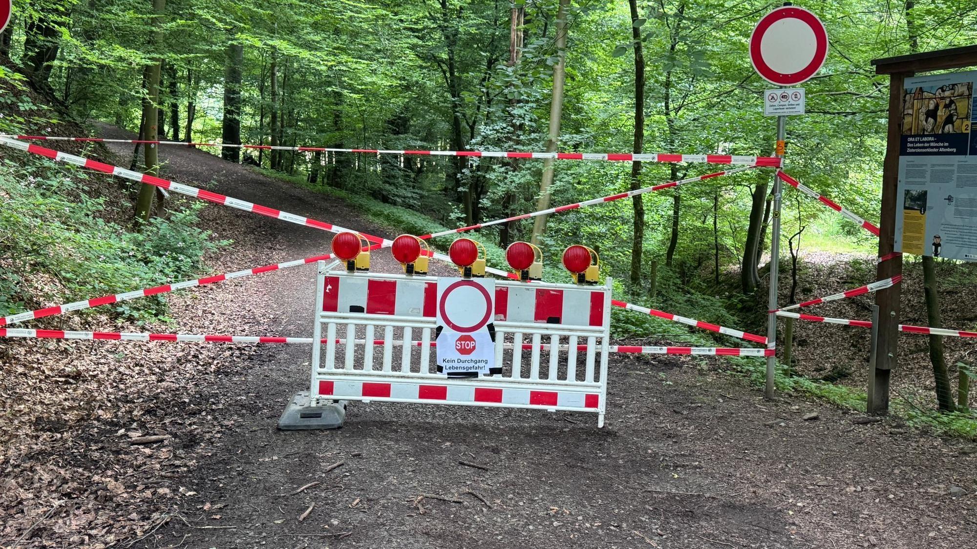 Eine weiß-rote Absperrbake vor einem Wanderweg. Darauf ein Schild mit der Warnung: "Kein Durchgang. Lebensgefahr!"