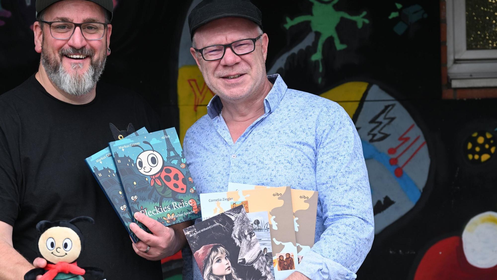 Zwei Männer halten Bücher in die Kamera, eines hat einen Marienkäfer auf dem Cover, ein anderes Rotkäppchen und Wolf