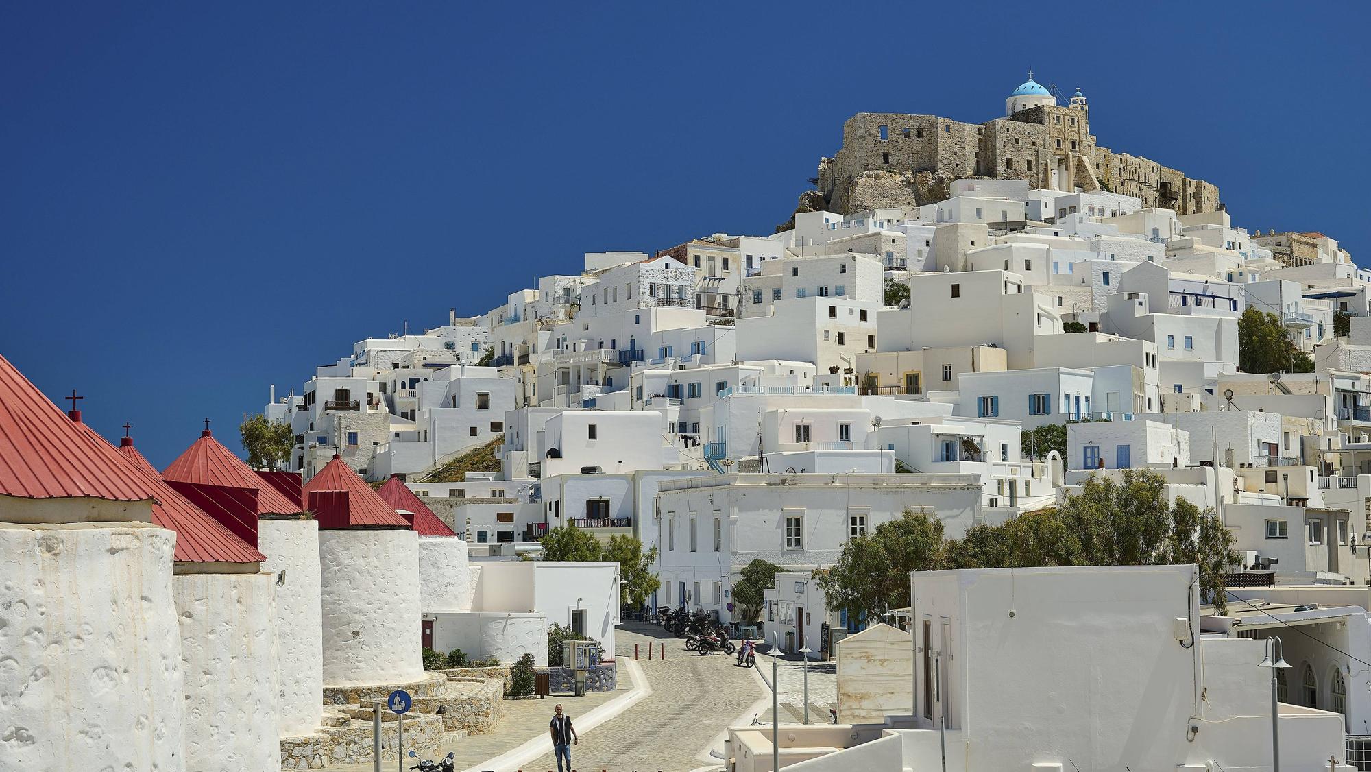 Blick auf die weiß getünchte Siedlung Chora mit den Windmühlen und der Burg Querini auf der griechischen Insel Astypalea unter strahlend blauem Himmel.