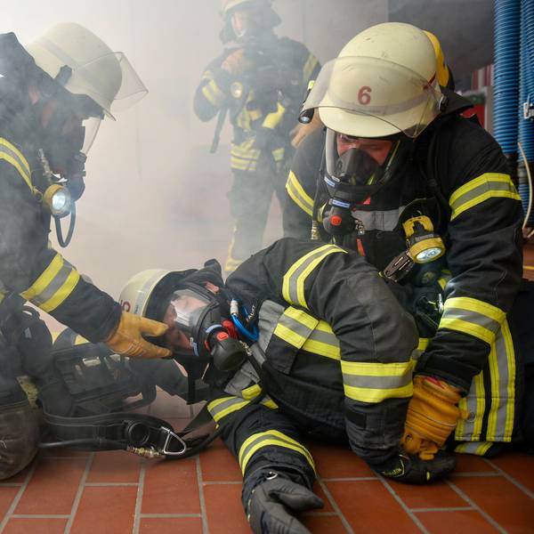 Das Bild zeigt Feuerwehrmänner mit Atemschutzmasken, die einen Kollegen retten.