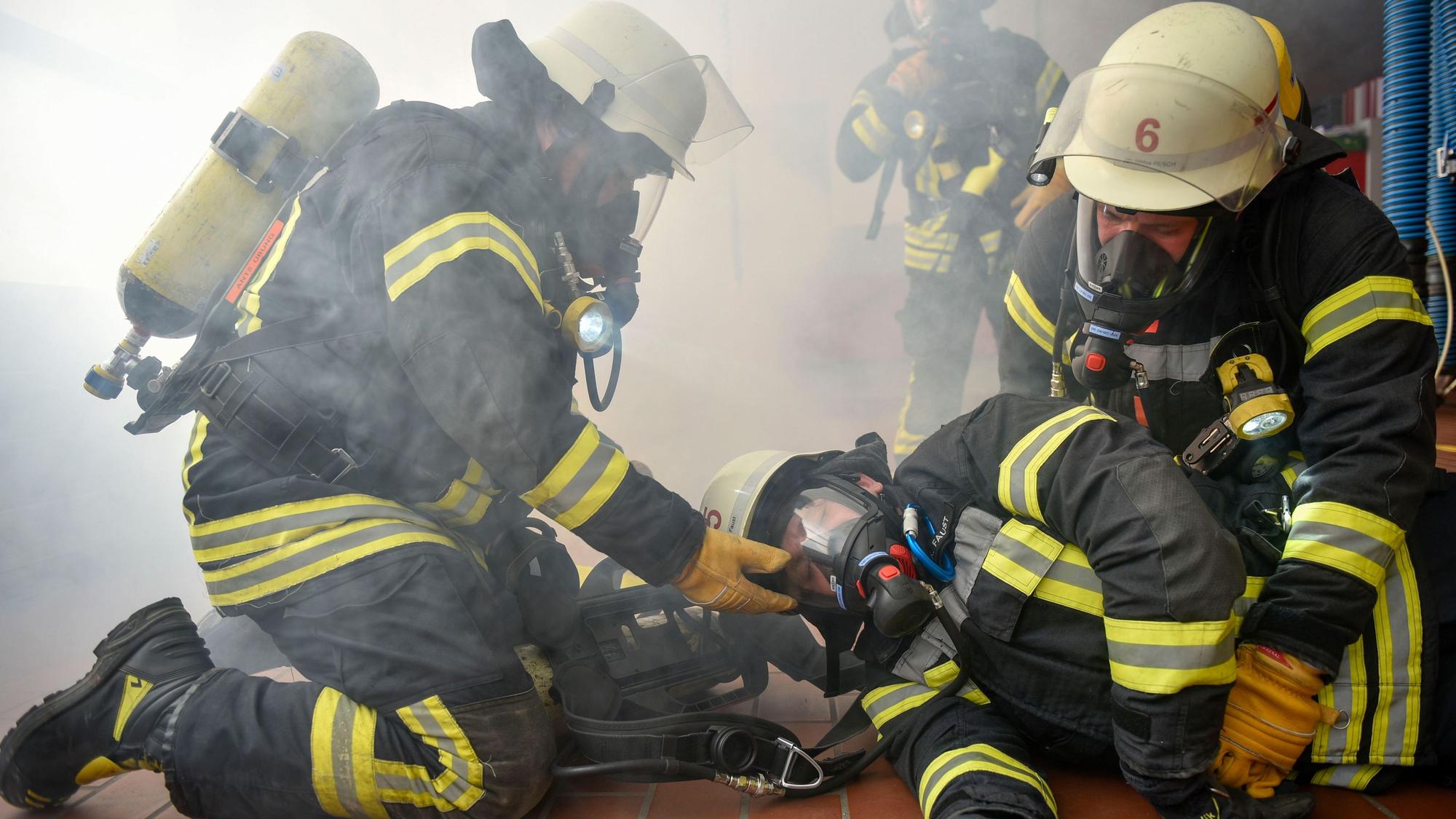 Das Bild zeigt Feuerwehrmänner mit Atemschutzmasken, die einen Kollegen retten.
