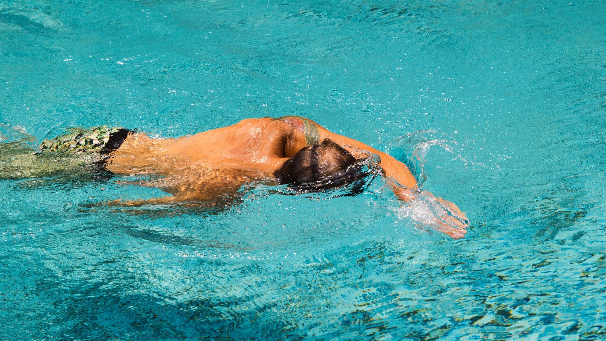 Ein junger Mann schwimmt an einem sonnigen Tag im klaren Wasser eines Schwimmbads.