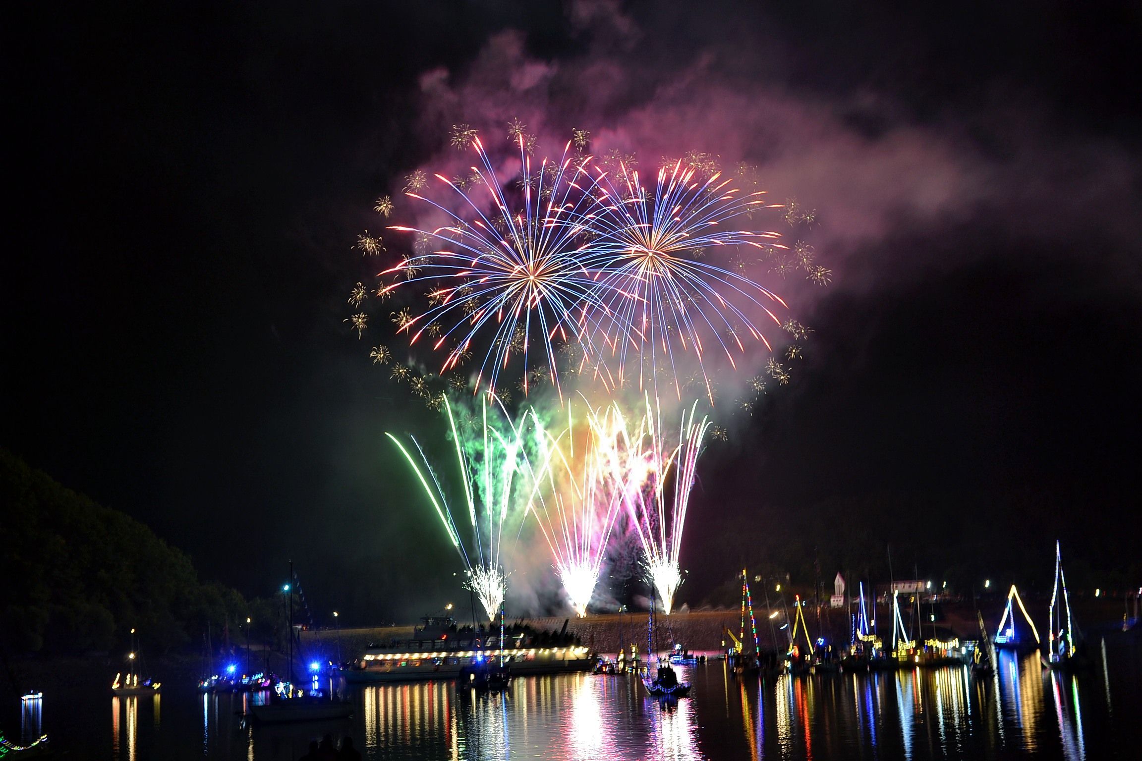 Feuerwerk explodiert am Nachtimmel und spiegelt sich im Wasser.