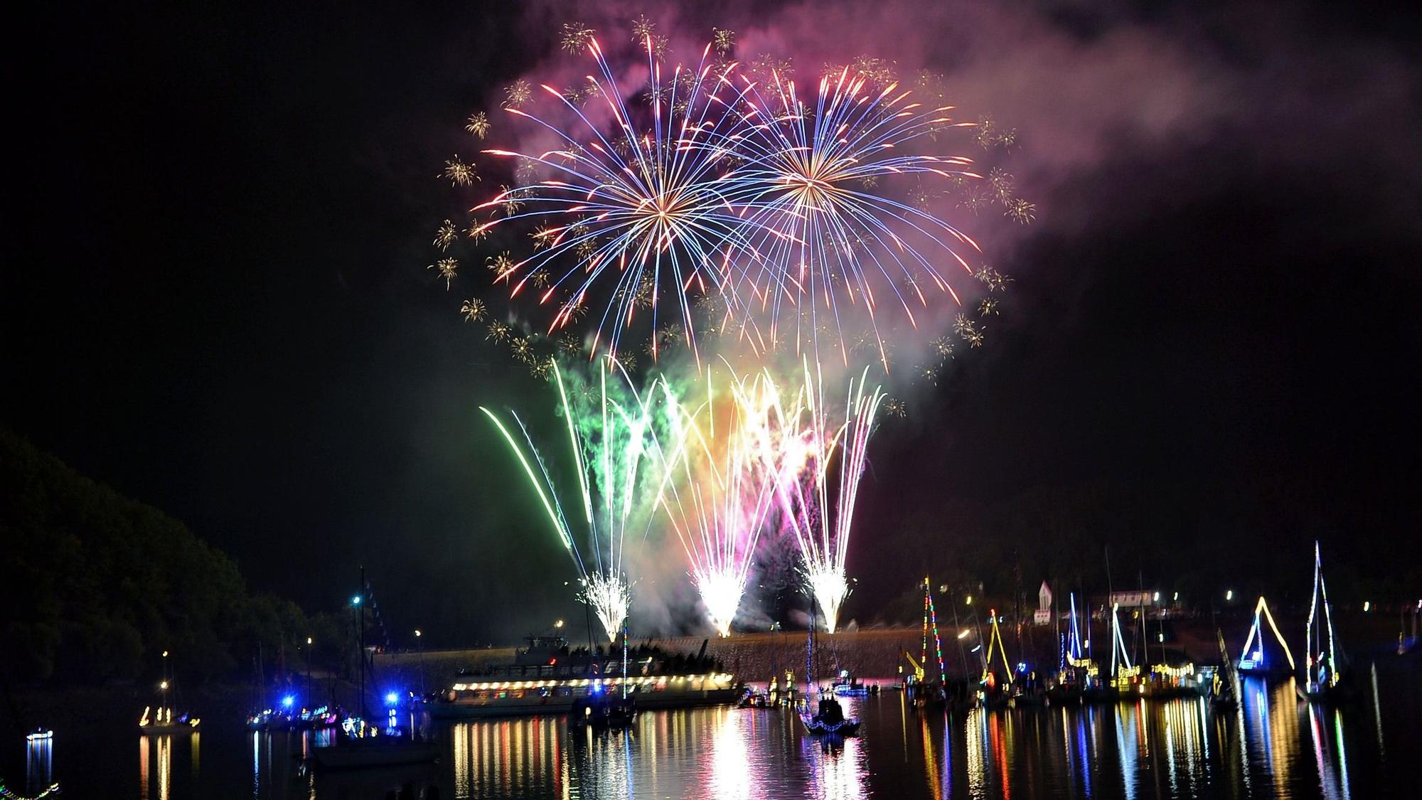 Feuerwerk explodiert am Nachtimmel und spiegelt sich im Wasser.