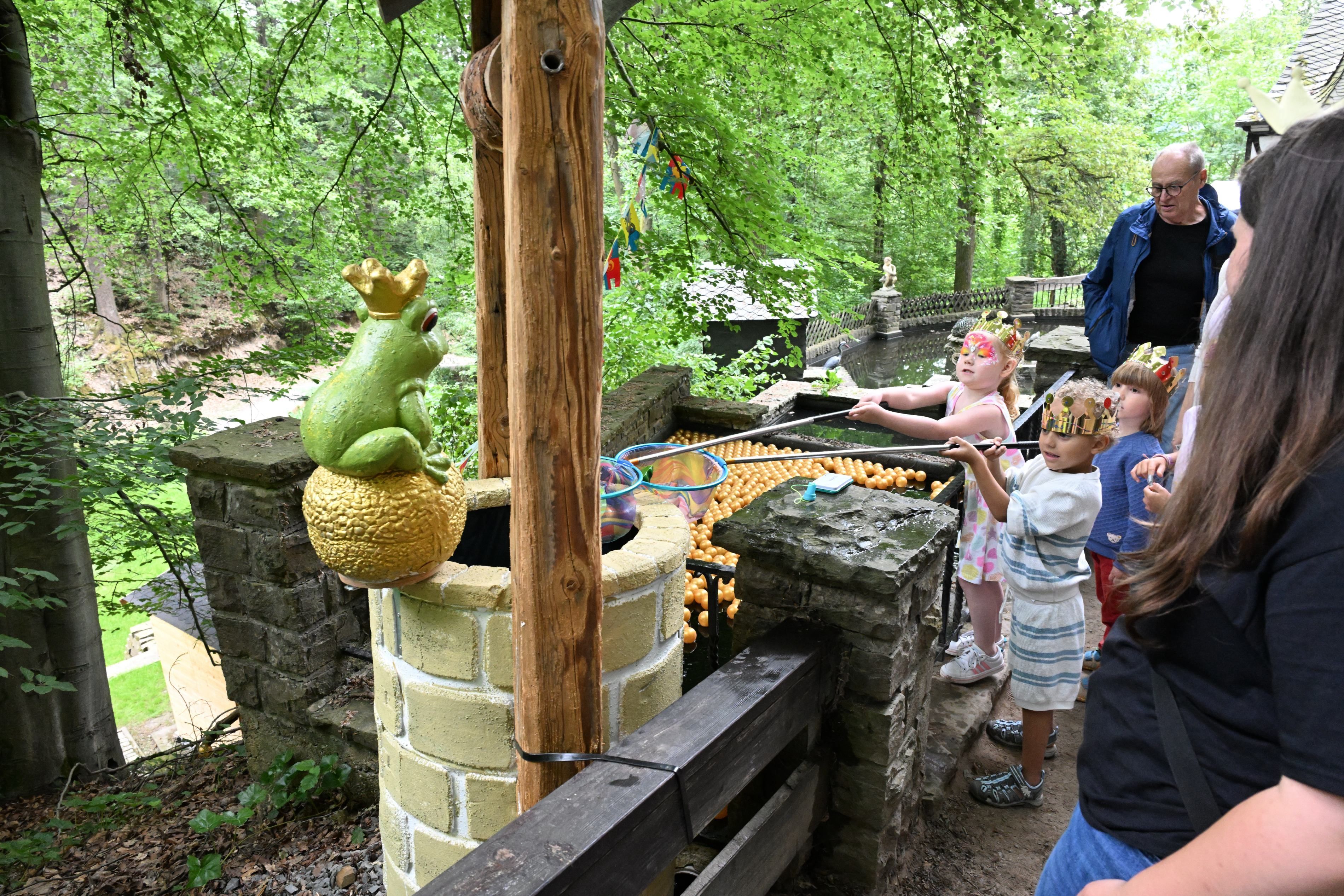Kinder mit Keschern vor einem Brunnen, auf dem ein großer Keramik-Froschkönig sitzt