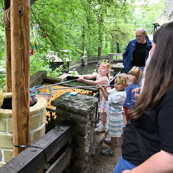 Kinder mit Keschern vor einem Brunnen, auf dem ein großer Keramik-Froschkönig sitzt