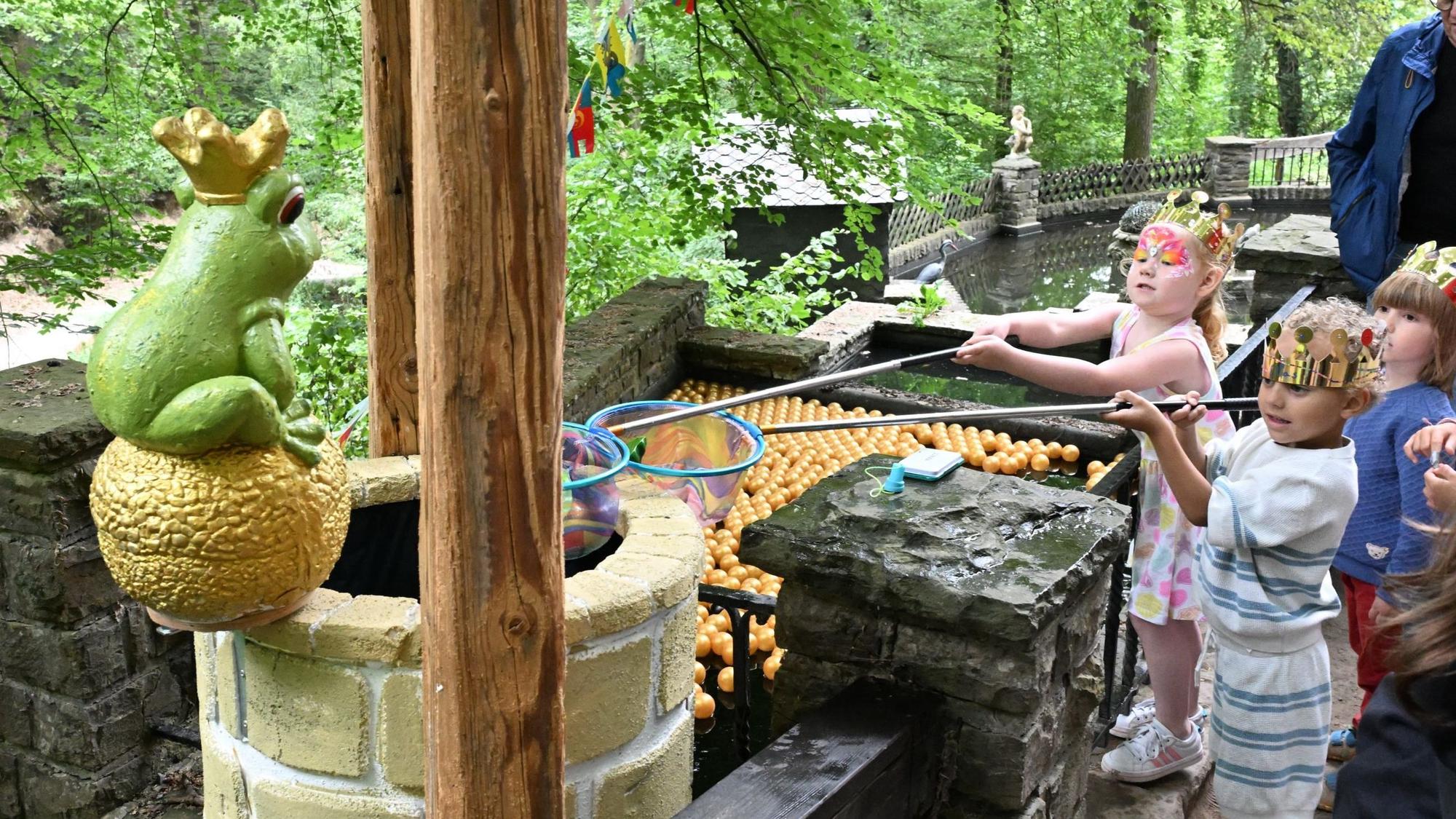 Kinder mit Keschern vor einem Brunnen, auf dem ein großer Keramik-Froschkönig sitzt