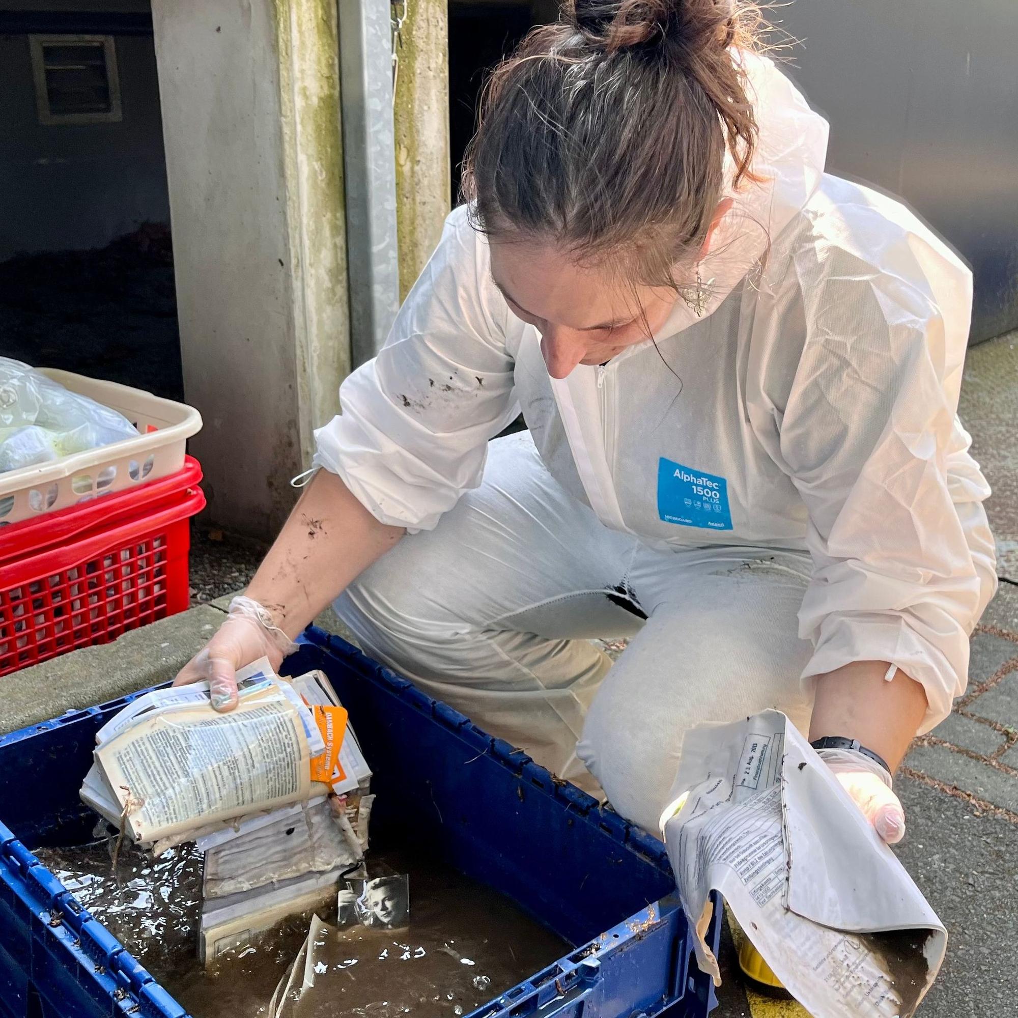 Eine Frau nimmt durchnässtes Papier aus einem mit Wasser befüllten Behälter.