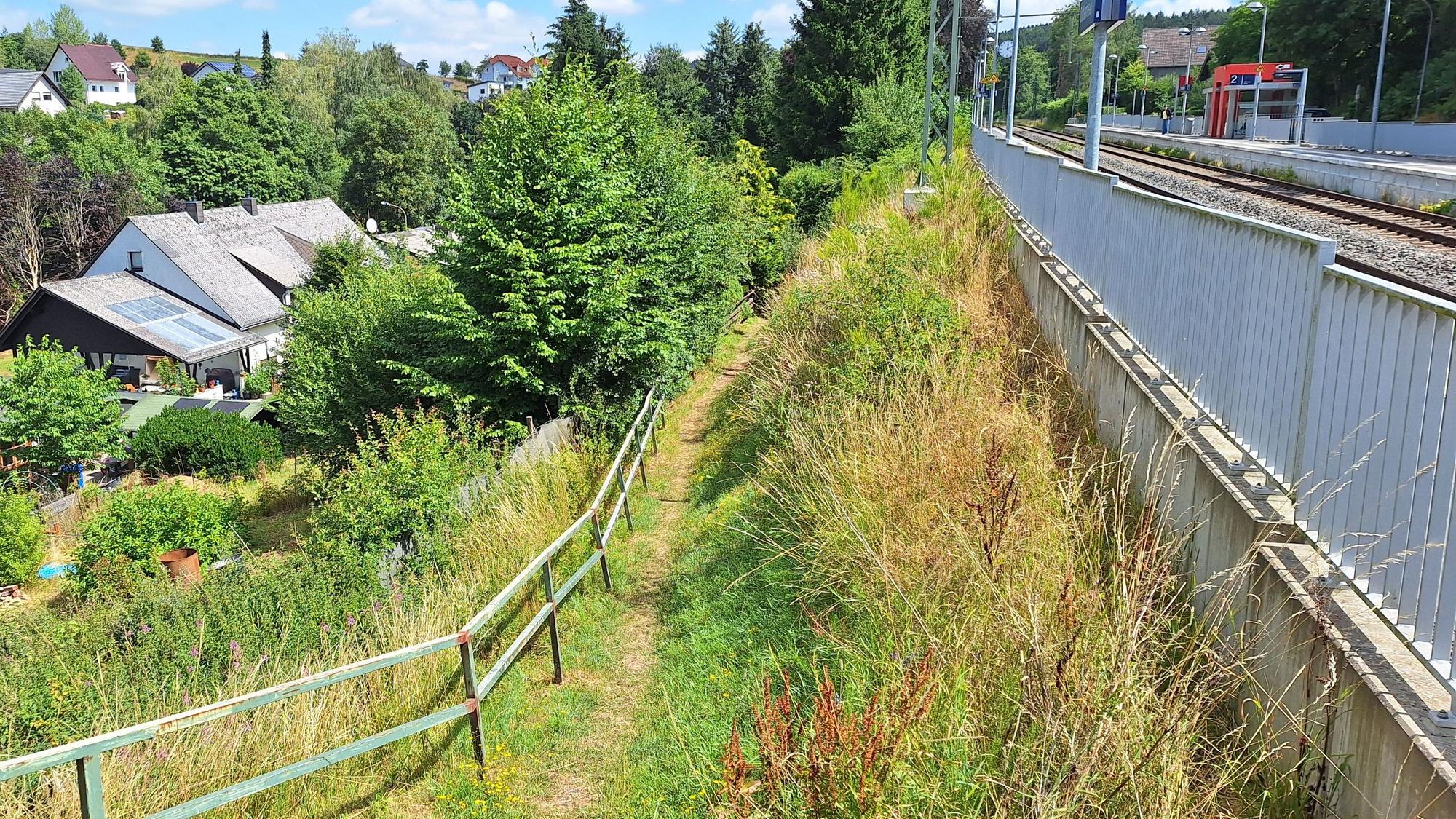 In der Bildmitte ist ein schmaler Pfad zu sehen, links Häuser eines Wohngebietes, rechts der Bahnhof in Dahlem.