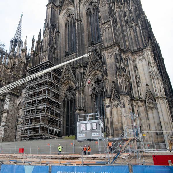 Vor dem Kölner Dom hängt eine Aufzugkabine am Haken eines Mobilkrans.