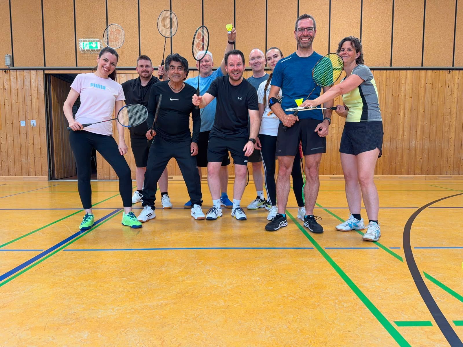 Frauen und Männer mit Badminton-Schlägern und Federbällen stehen in einer Halle.