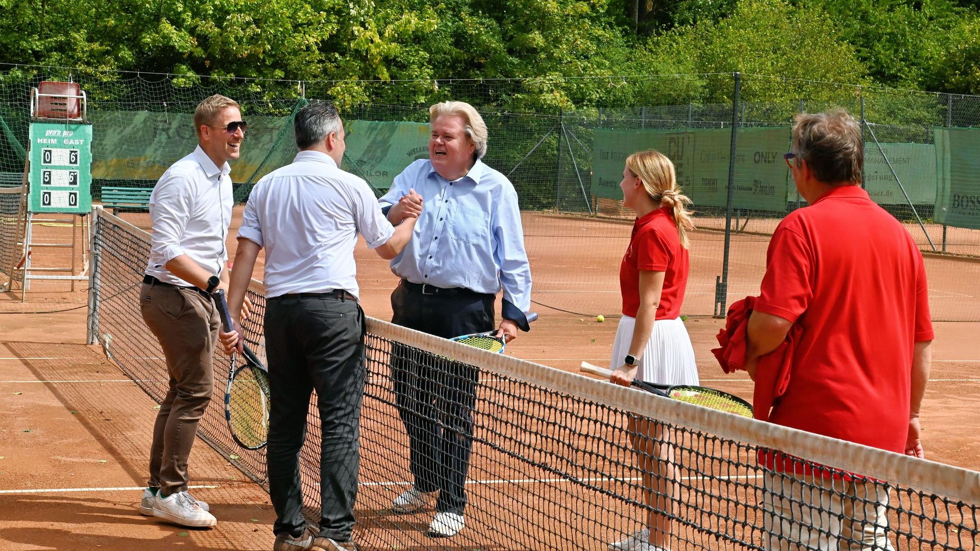 Markus Ramers, Klaus Voussem und Sacha Reichelt stehen auf dem Tennisplatz am Netz, neben ihnen zwei Vereinsmitglieder.