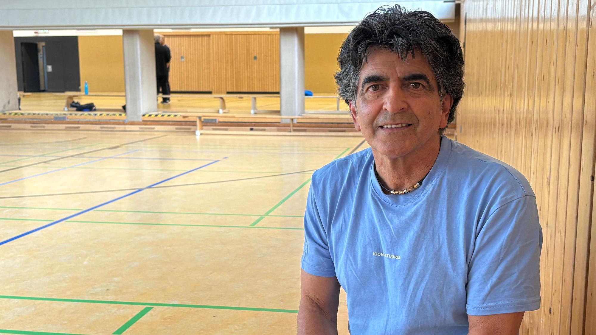 Ein Mann sitzt in einer Sporthalle.