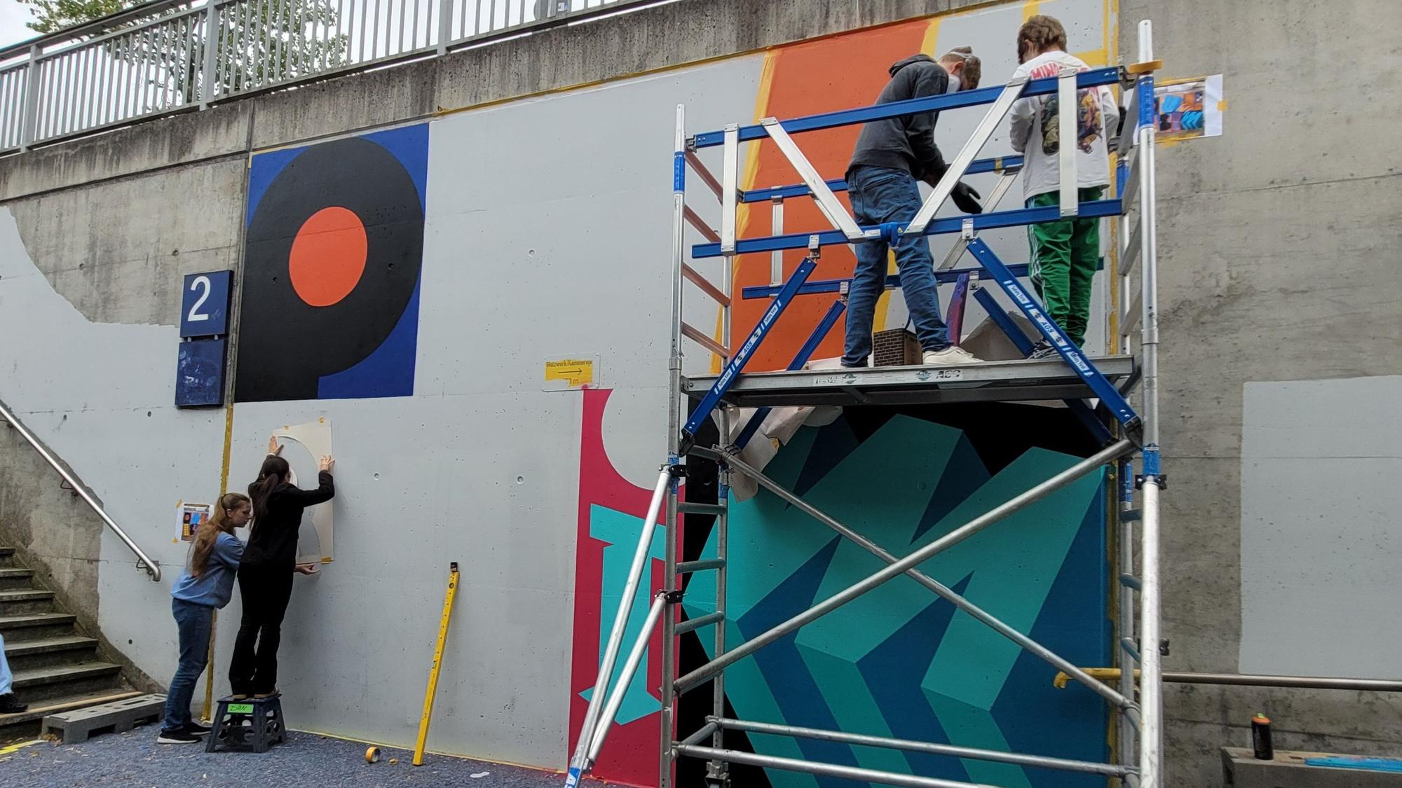 Jugendliche gestalten eine Wand mit bunten Farben.