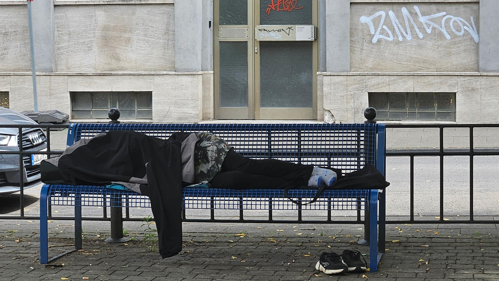 Ein Mann schläft auf einer Bank auf dem Spielplatz.