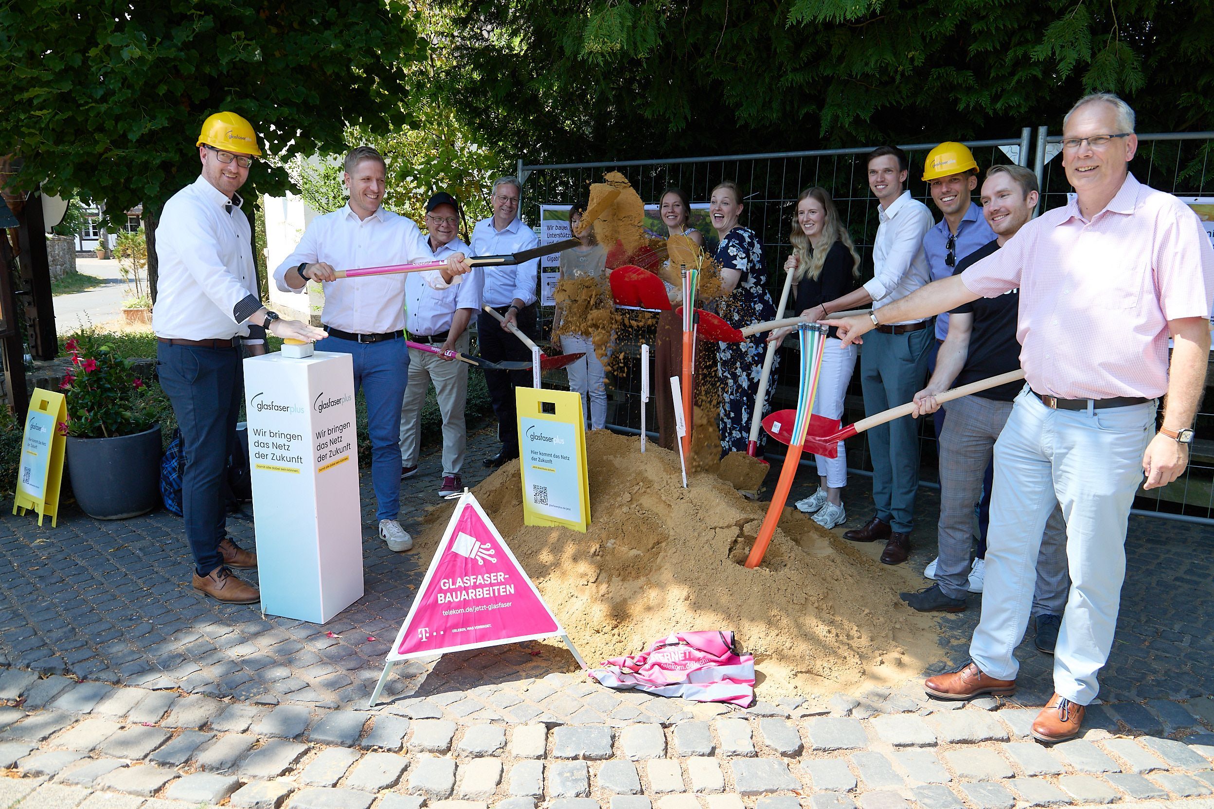 Die Vertreter der Kommunen und der beteiligten Firmen haben sich im Halbkreis um einen Sandhügel gruppiert, um mit Schaufeln den ersten Spatenstich durchzuführen.